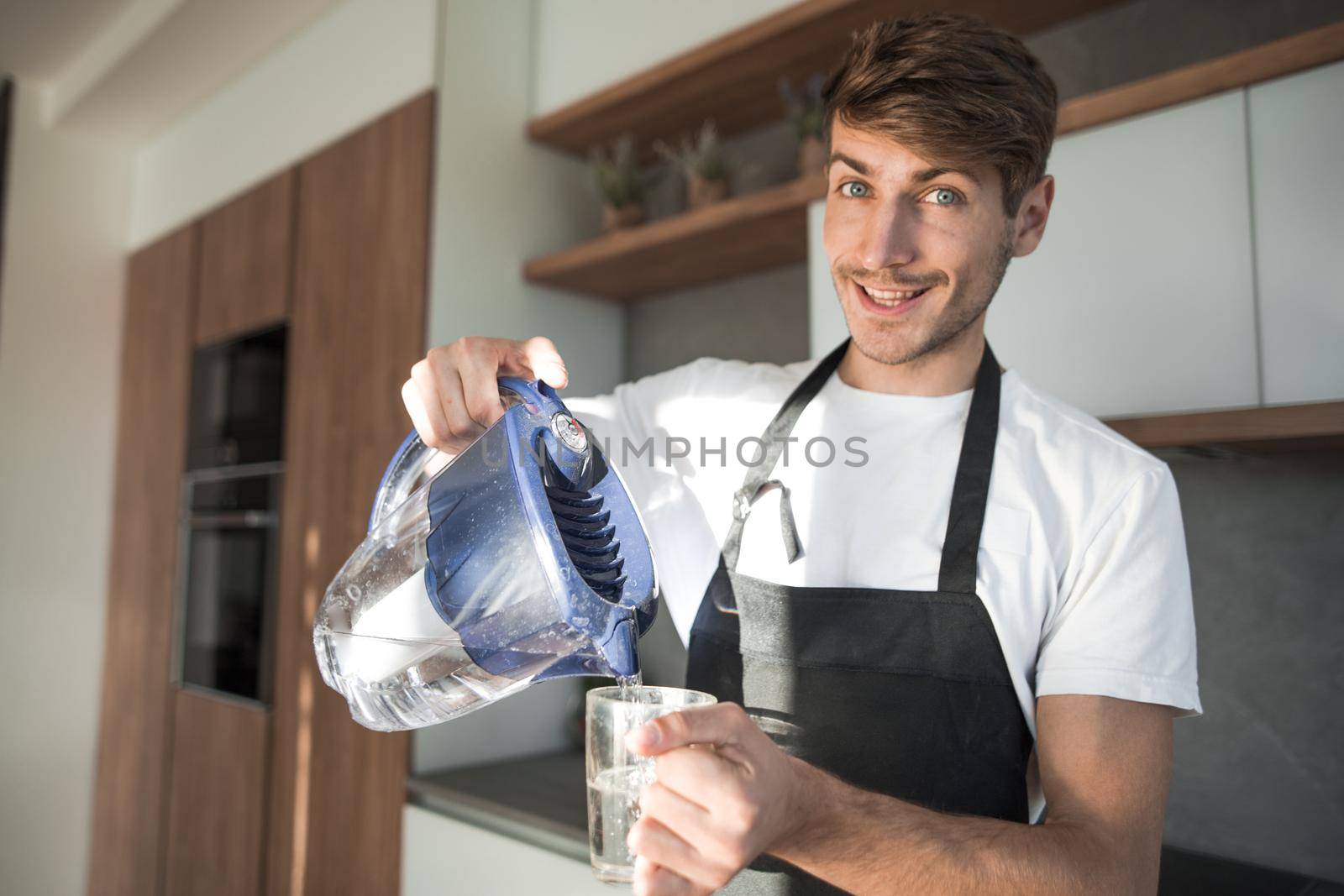 smiling young man pours drinking water into a glass by asdf
