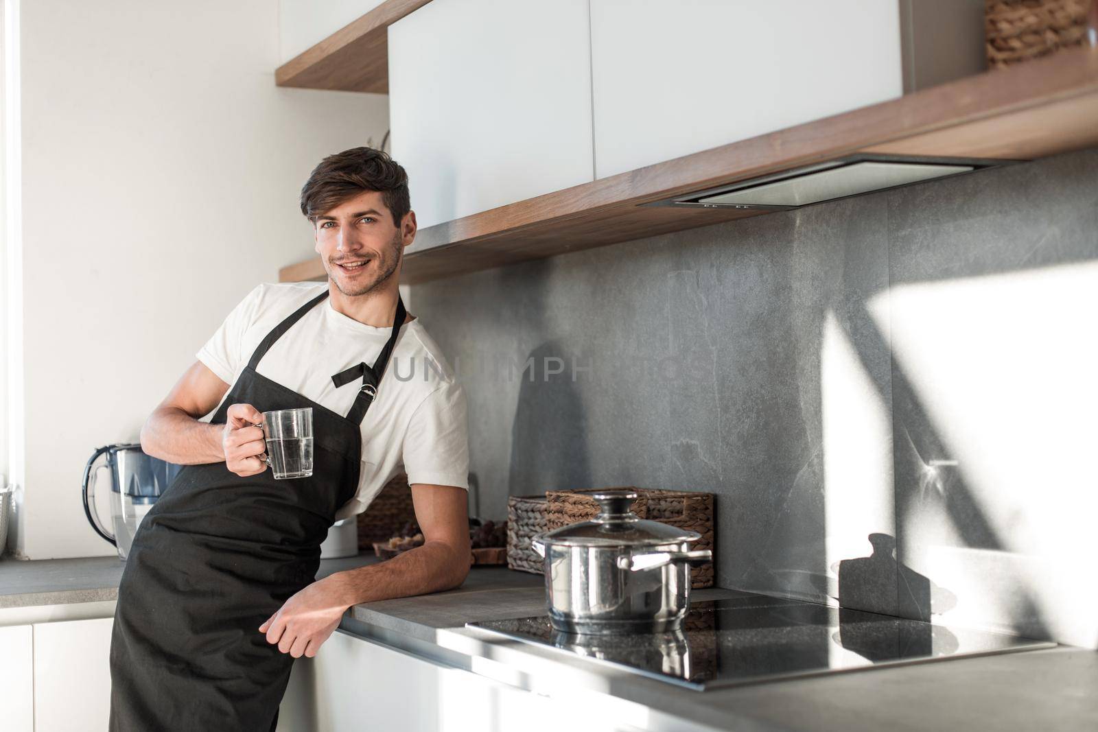smiling young man with a glass of water standing in the home kitchen. photo with copy space
