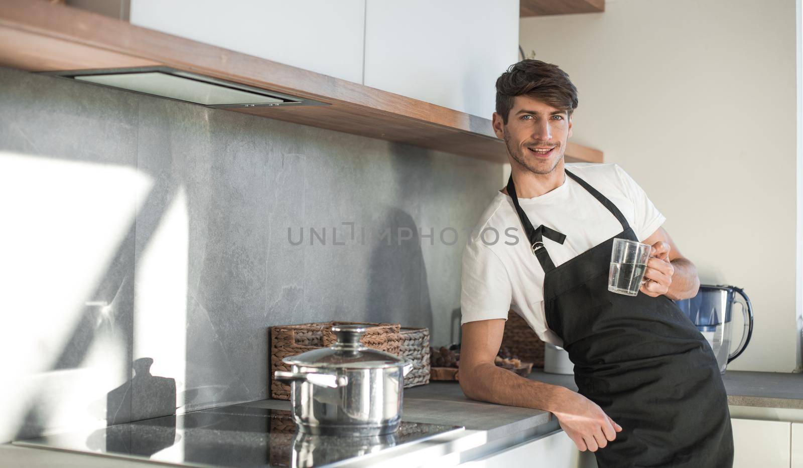 smiling young man with a glass of water standing in the home kitchen. photo with copy space