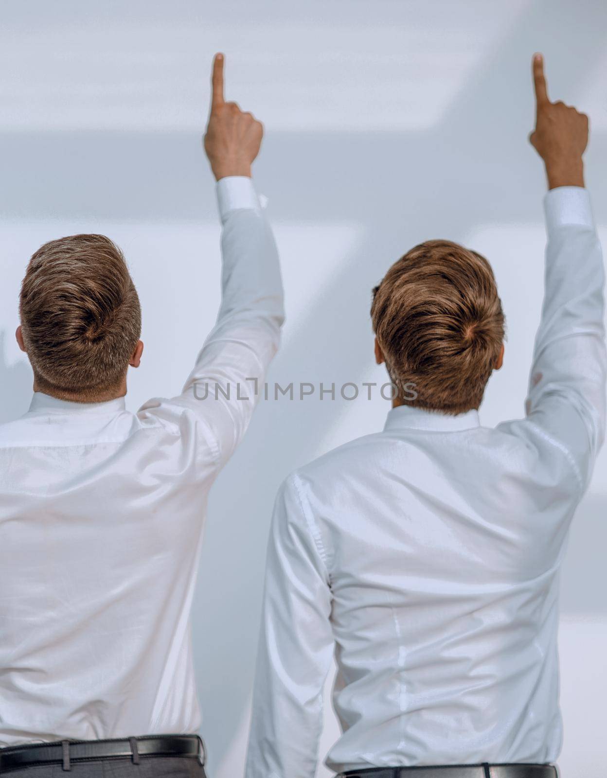 two young people stand with their backs to the camera and point with their thumbs up