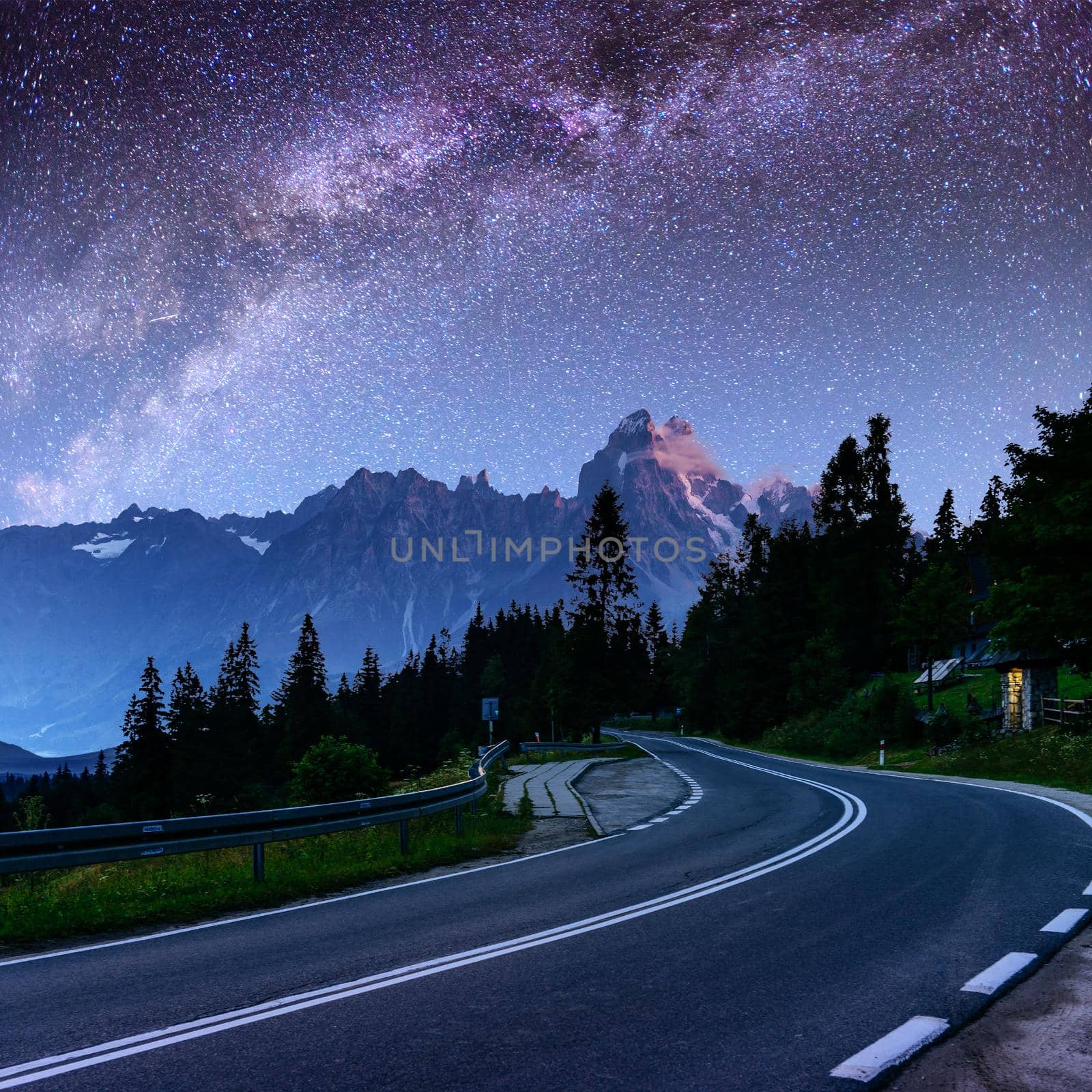 Starry Sky over the mountains. The asphalt road with white markings. Beautiful summer landscape. Soft filtering effect. Europe