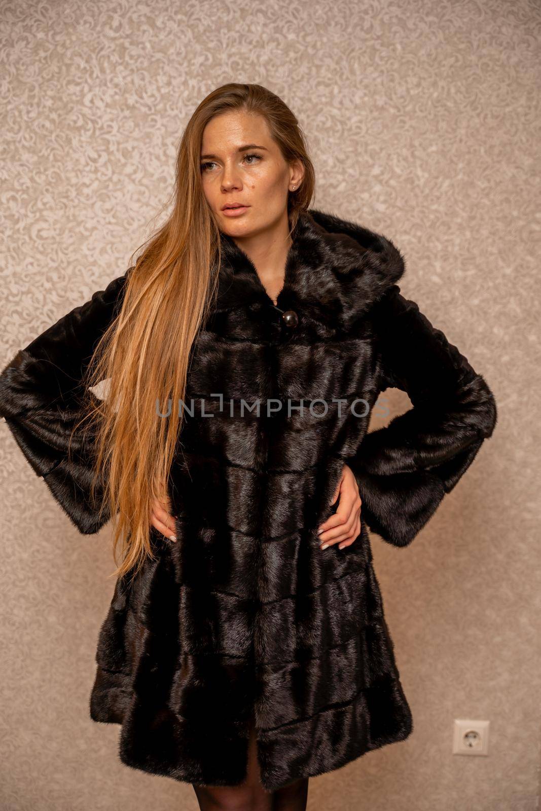 Young beautiful glamorous woman in a black luxurious fur coat posing against the background of a golden wall. fashion portrait.