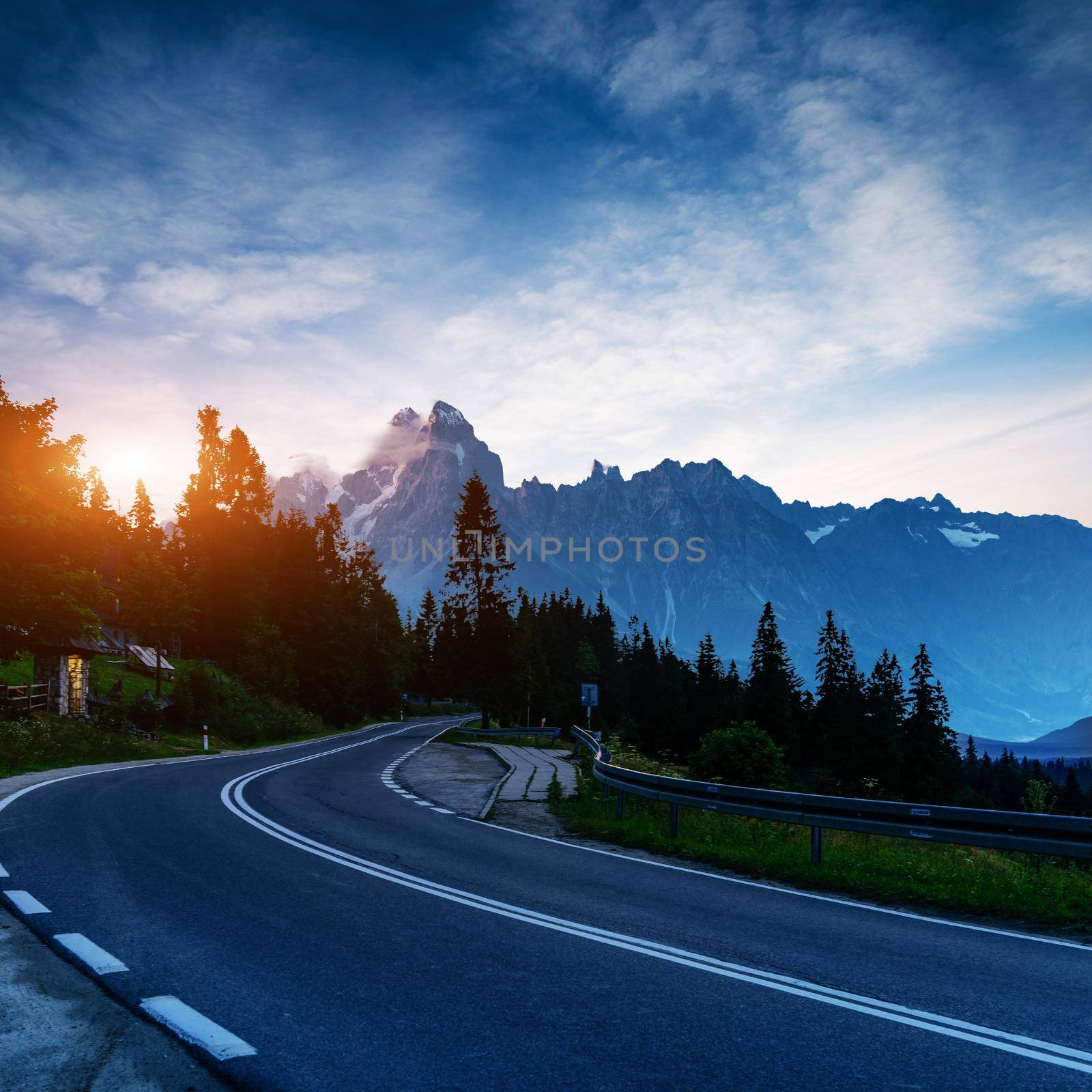 Fantastic sunset that leads into the mountains. Asphalt road with white markings. Beautiful summer landscape. Soft filtered effect. Europe