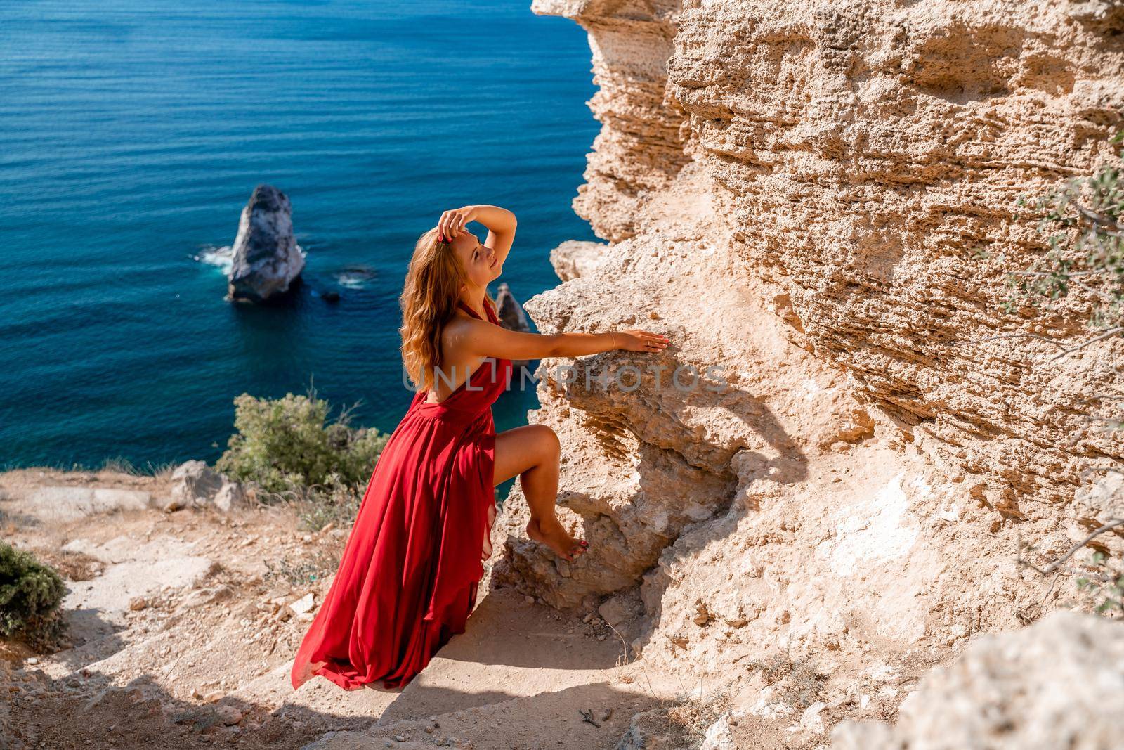 A woman in a red flying dress fluttering in the wind, against the backdrop of the sea