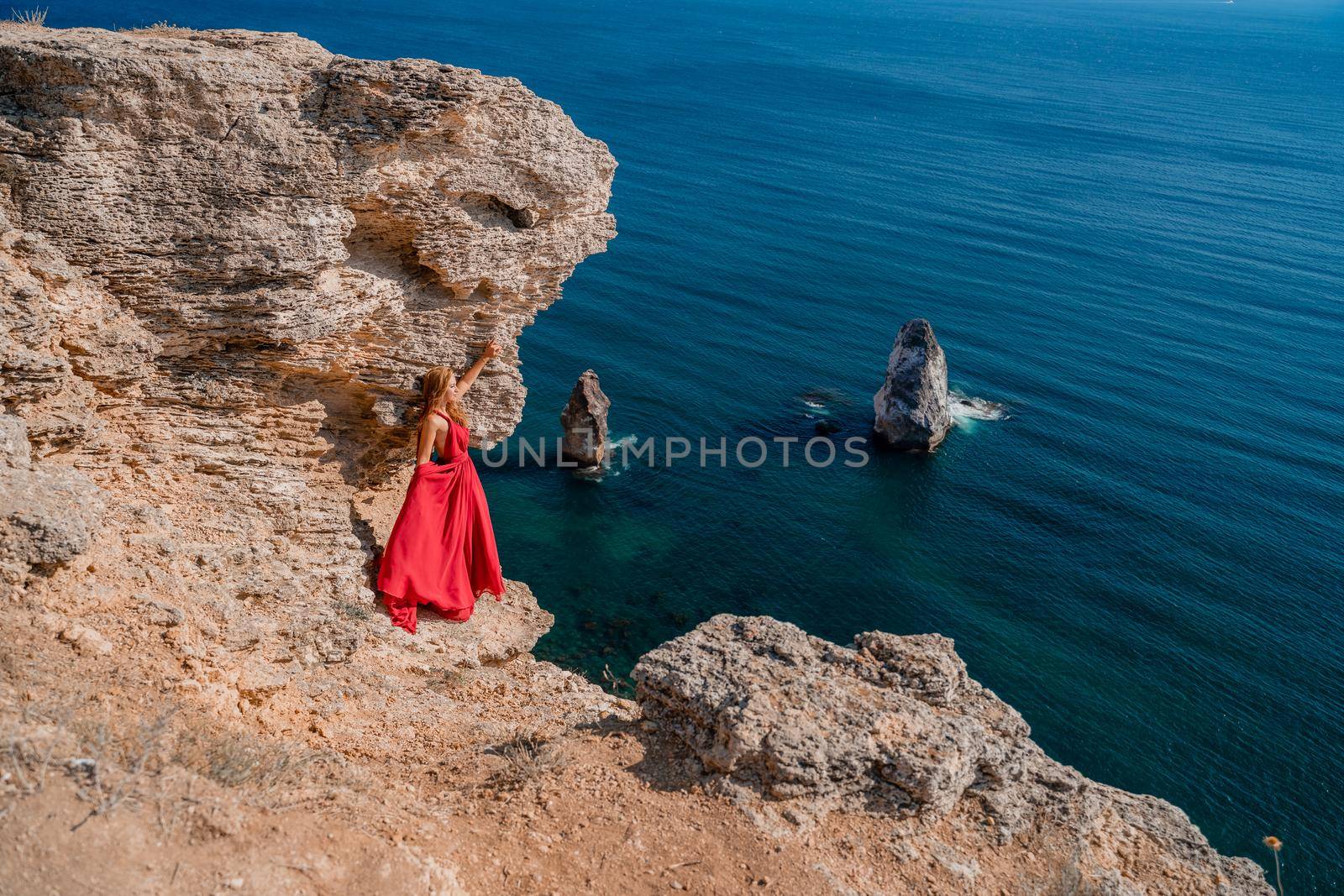 A woman in a red flying dress fluttering in the wind, against the backdrop of the sea