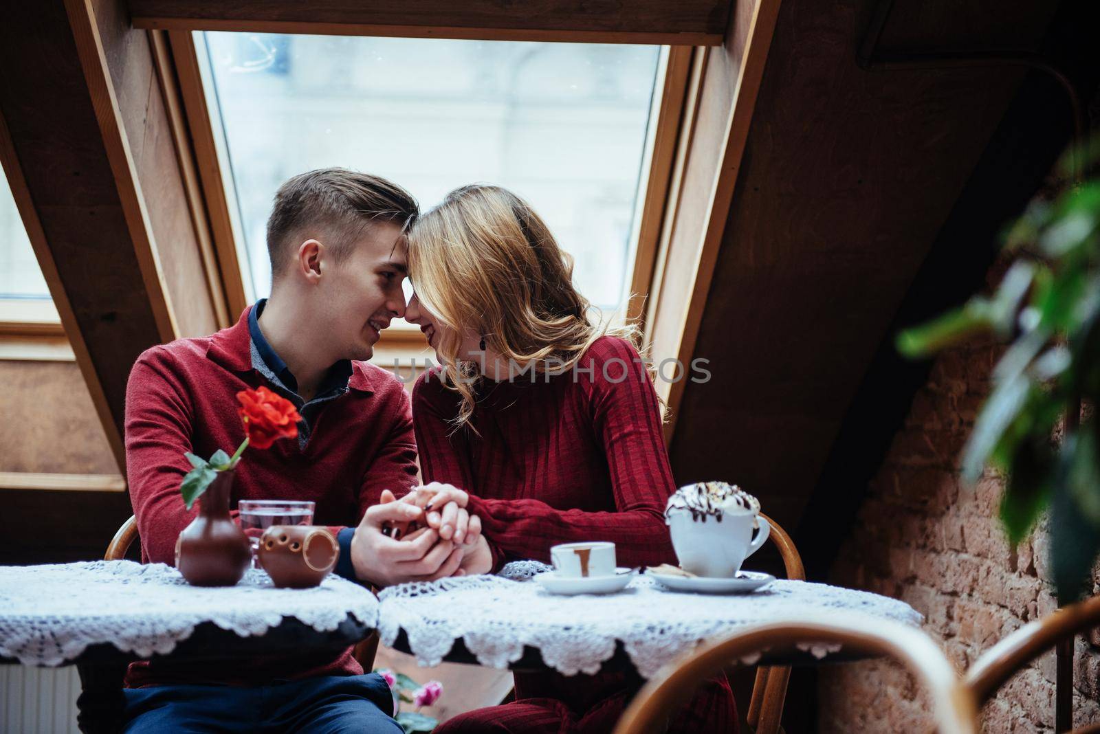 Beautiful young man and woman are celebrating Valentine day at restaurant. The man is giving a rose to his girlfriend