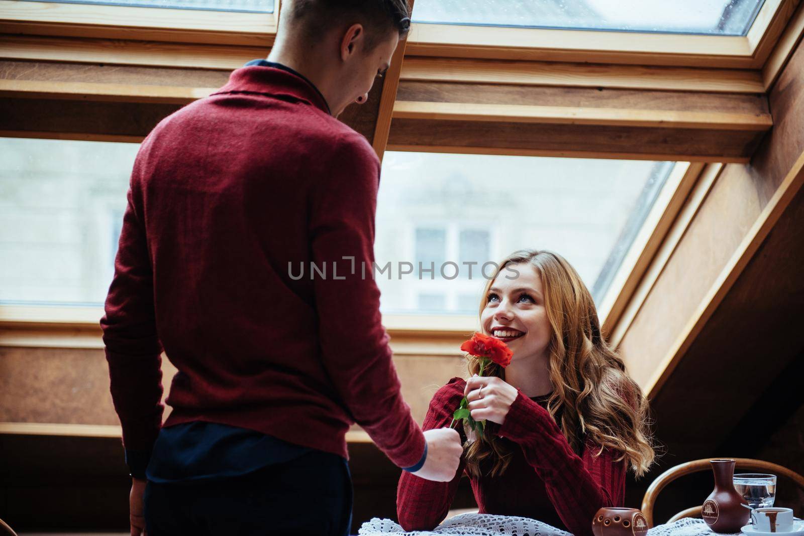 Beautiful young man and woman are celebrating Valentine day at restaurant. The man is giving a rose to his girlfriend