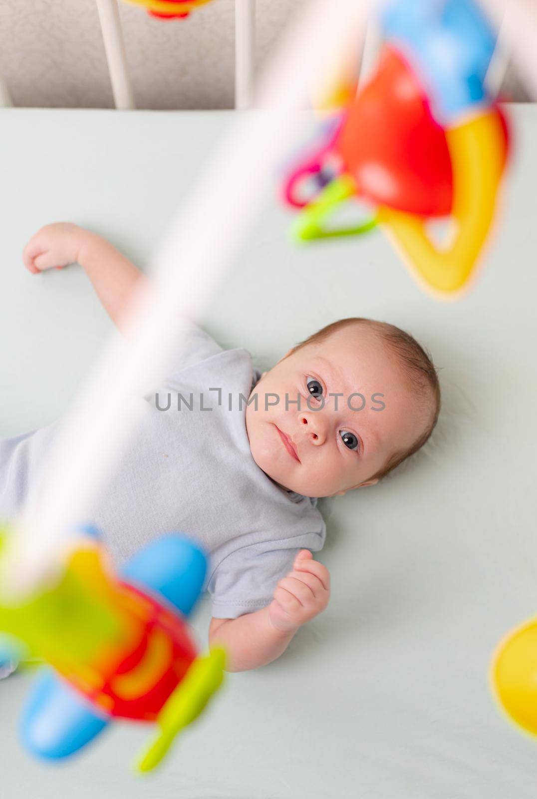 The baby looks at the mobile lying in the crib . Mobile to the crib. An article about kids' leisure. Mom's hands are free. An article about choosing a mobile in the crib. The baby is 0-3 months old. An infant