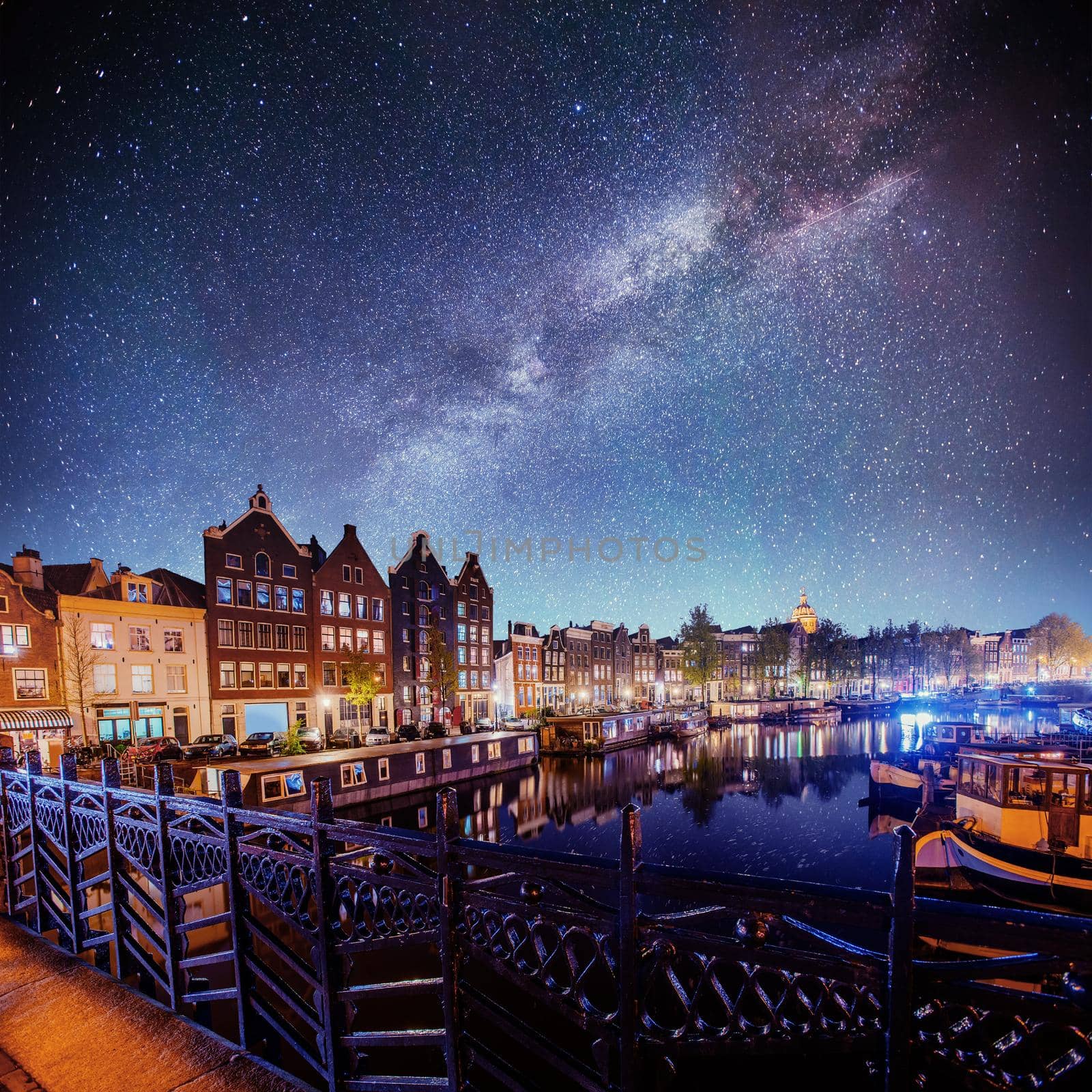 Beautiful night in Amsterdam. Night illumination of buildings and boats near the water in the canal.