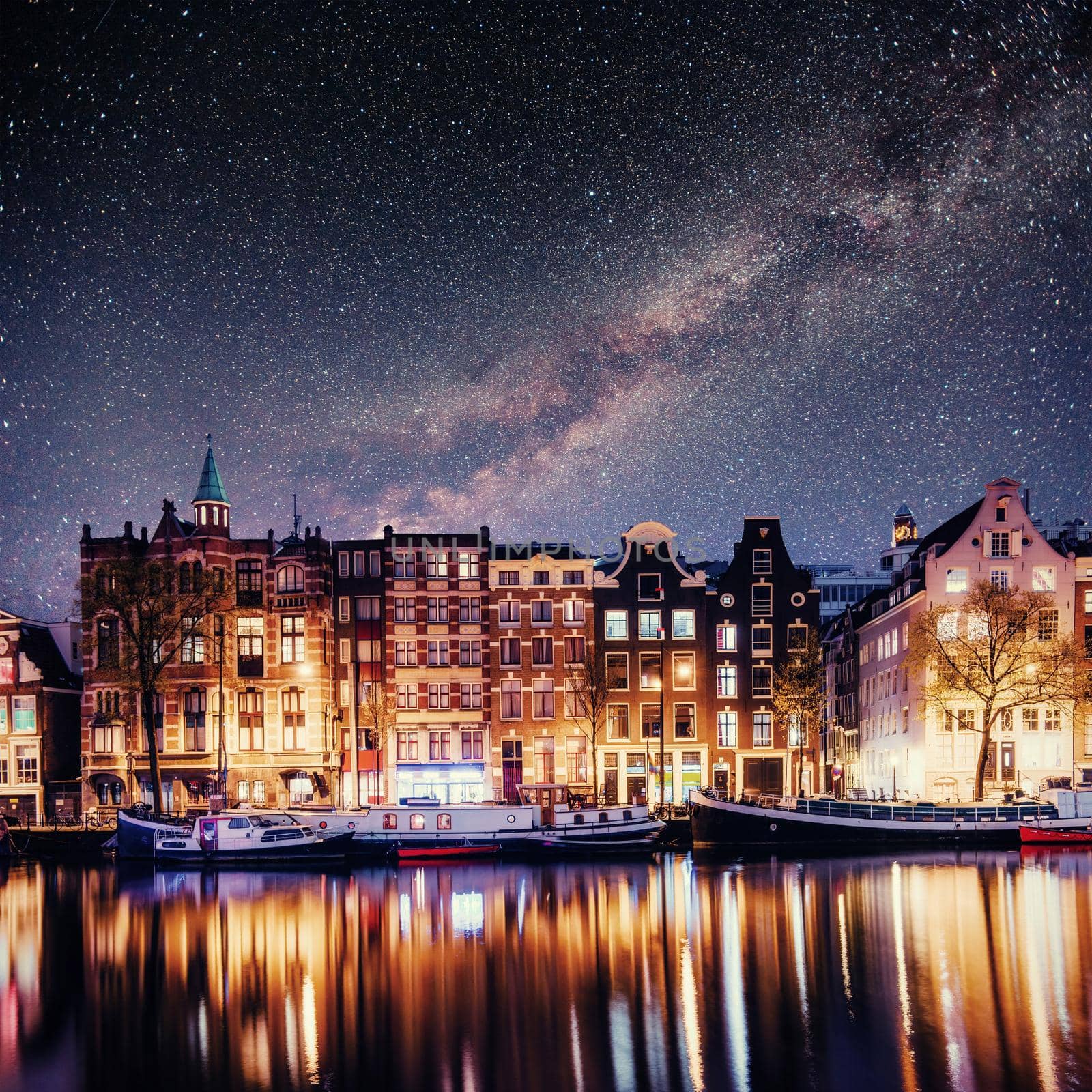 Beautiful night in Amsterdam. Night illumination of buildings and boats near the water in the canal.