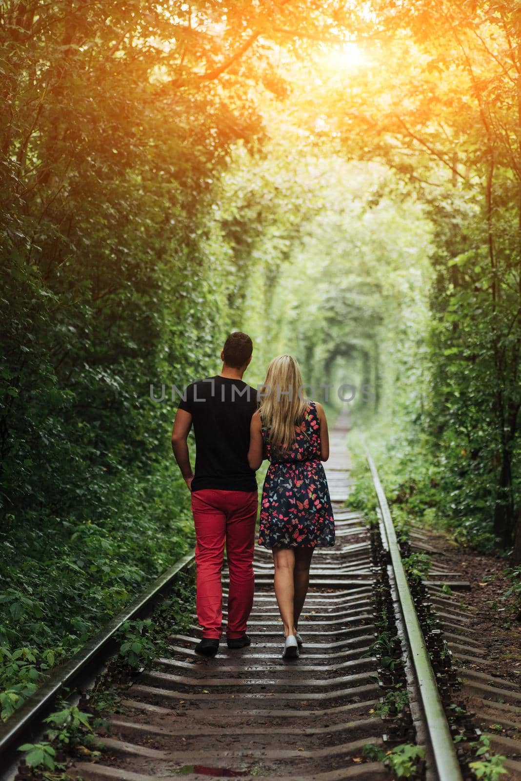Loving couple in a tunnel of green trees on railroad by Standret