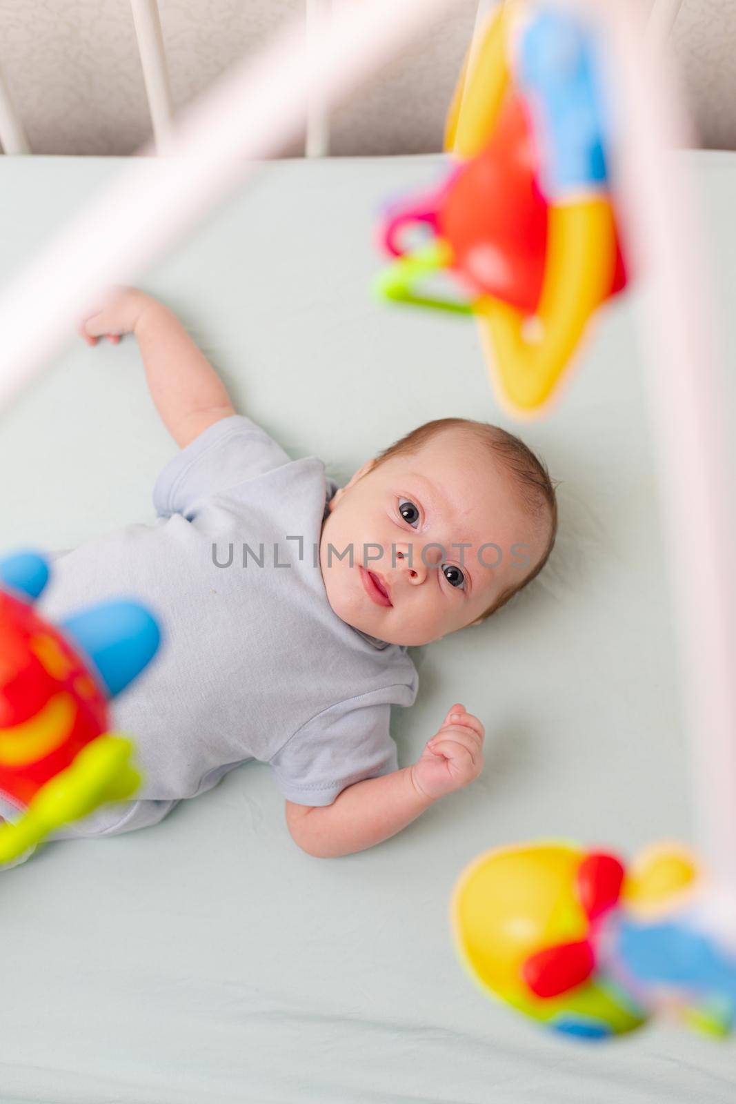 The baby looks at the mobile lying in the crib . Mobile to the crib. An article about kids' leisure. Mom's hands are free. An article about choosing a mobile in the crib. The baby is 0-3 months old. An infant