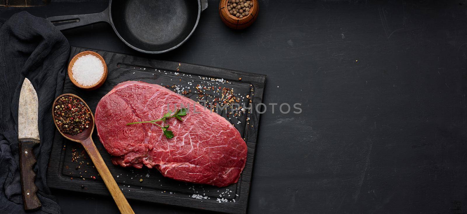 Raw beef tenderloin lies on a cutting board and spices for cooking on a black table, top view by ndanko