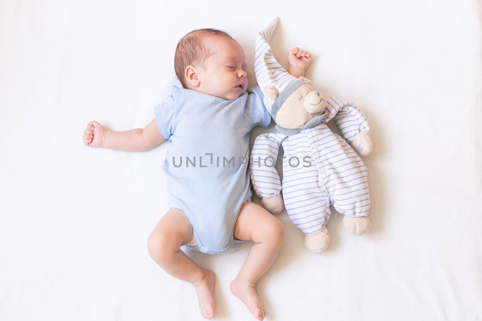 The baby is lying in a crib with a teddy bear . The baby is 0-3 months old. A calm sleeping baby. Healthy baby sleep. An article about toys for kids. A soft toy. Copy Space