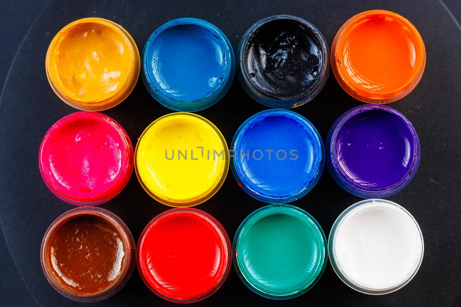 full-frame close-up background of opened small gouache paint jars on black