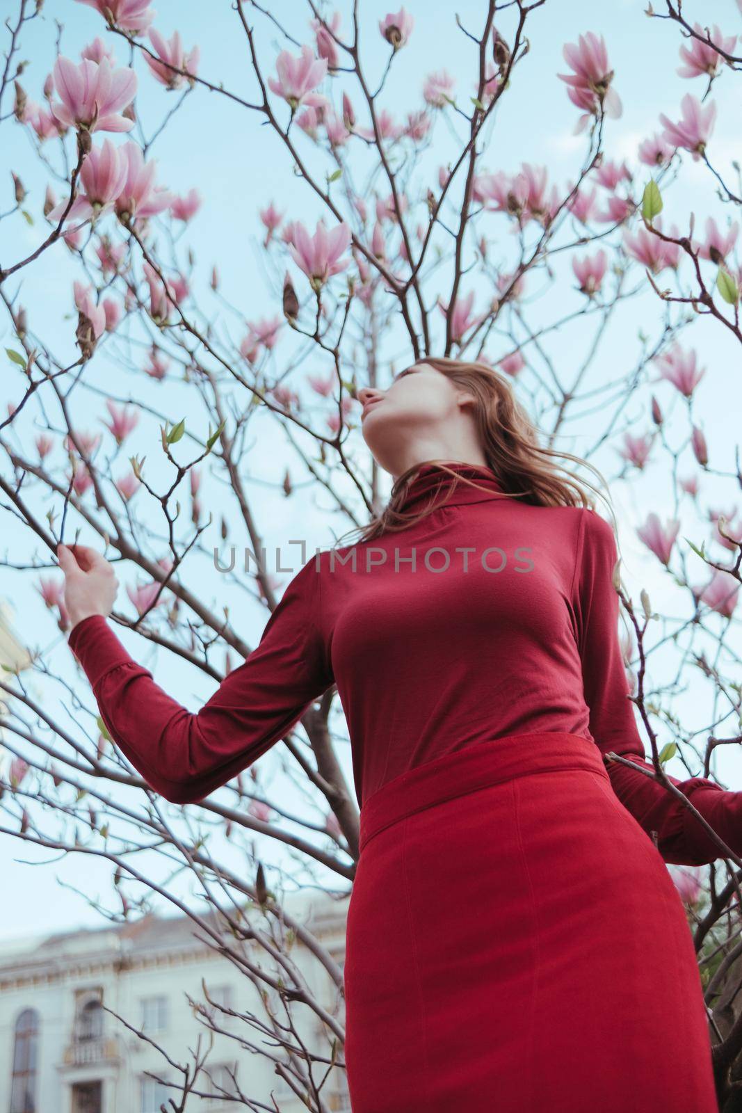 a veth-haired girl in red against the background of a magnolia tree. the concept of unity with nature