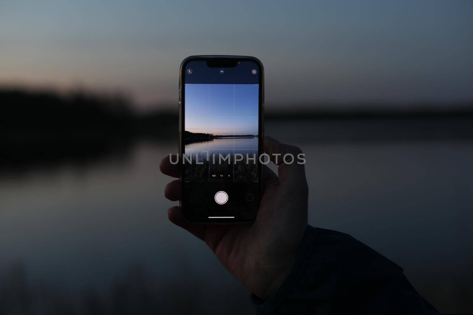 hands holding mobile phone at sunset and taking photo of beautiful nature