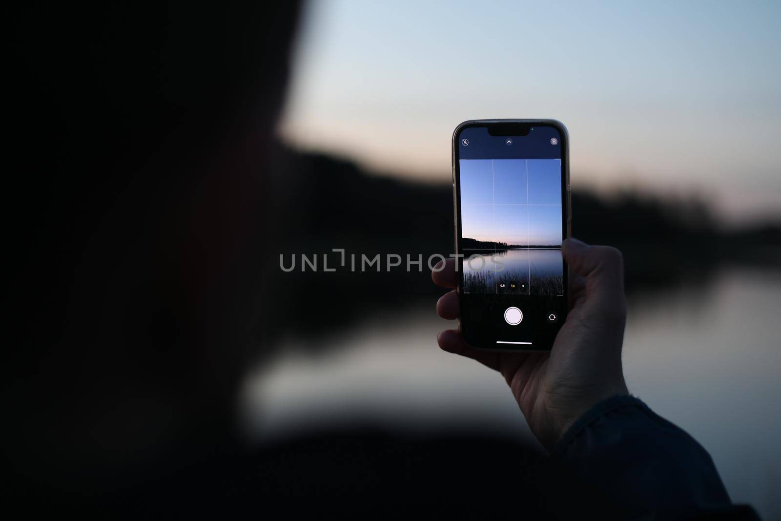 hands holding mobile phone at sunset and taking photo of beautiful nature
