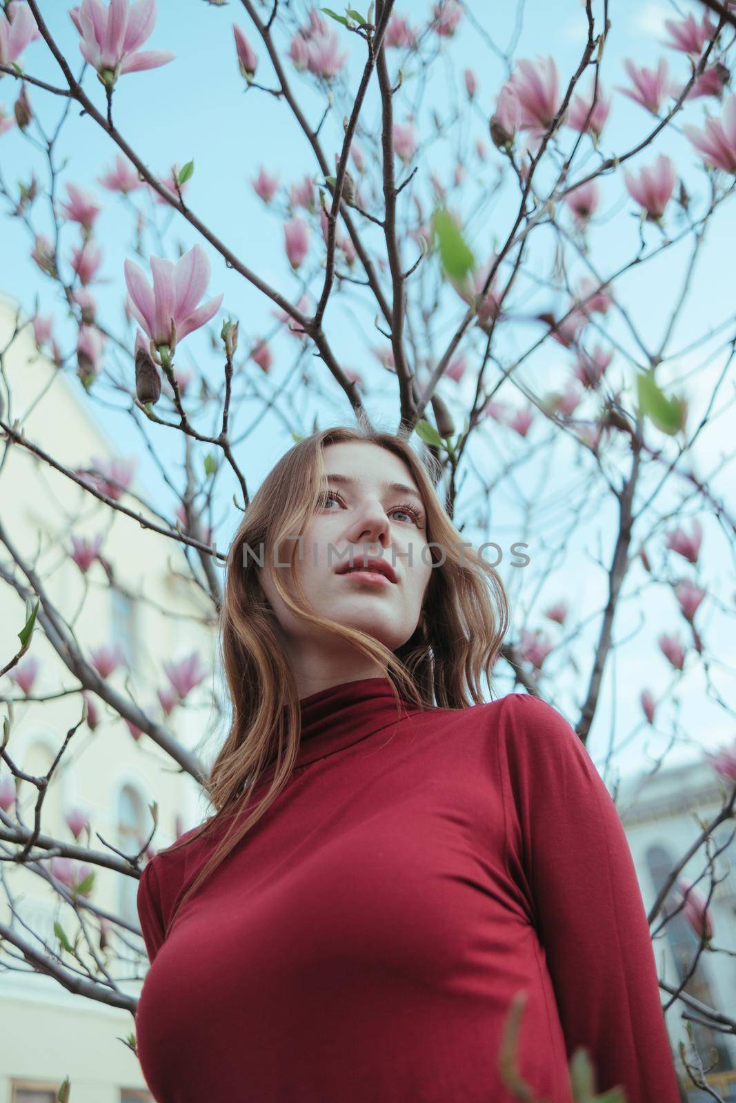 a veth-haired girl in red against the background of a magnolia tree. the concept of unity with nature by Symonenko