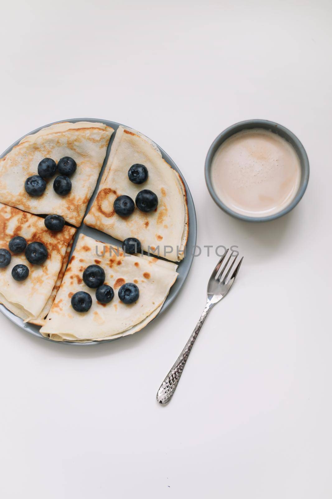 breakfast with a cup of cappuccino and pancakes with berries on a white background top view.