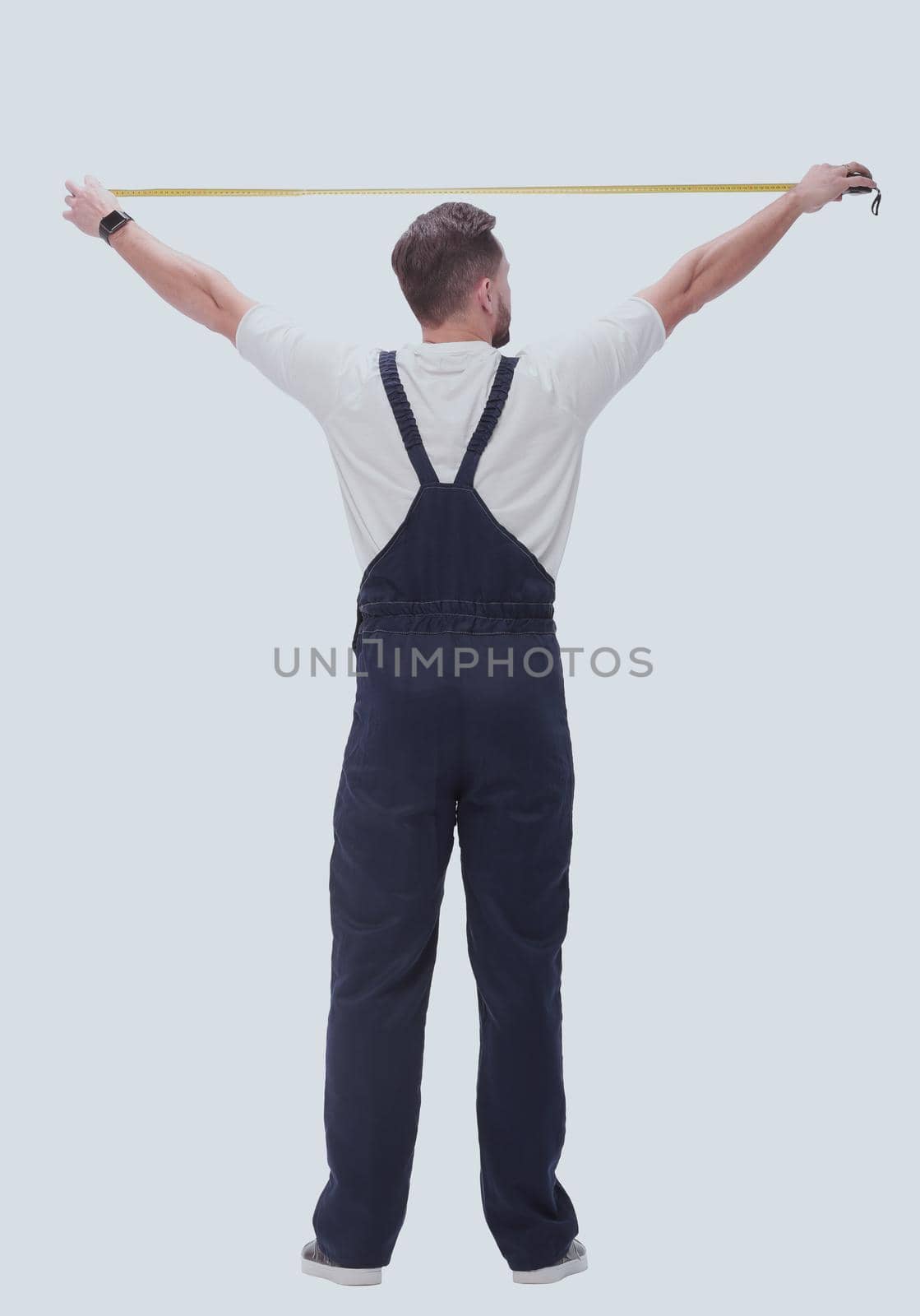 rear view. a man measuring something with a construction tape measure. isolated on white background