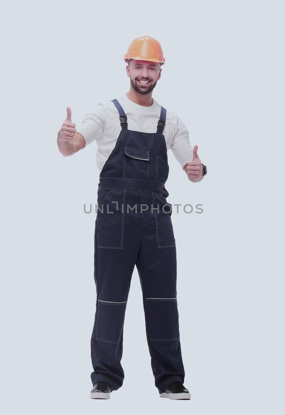 in full growth. smiling man in overalls showing thumbs up . isolated on white background