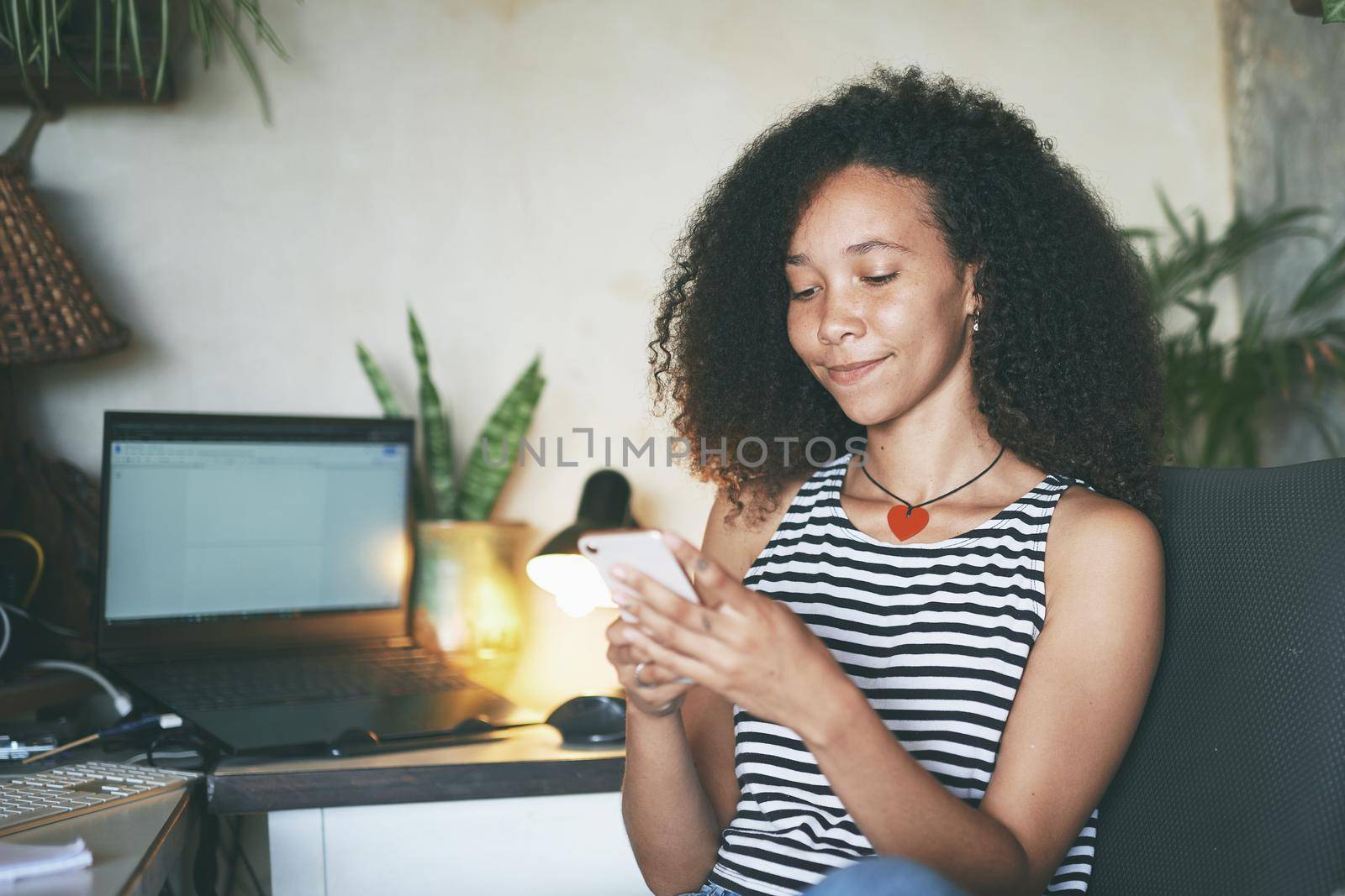 Shot of an attractive young woman sitting alone and using her cellphone to work from home stock photo