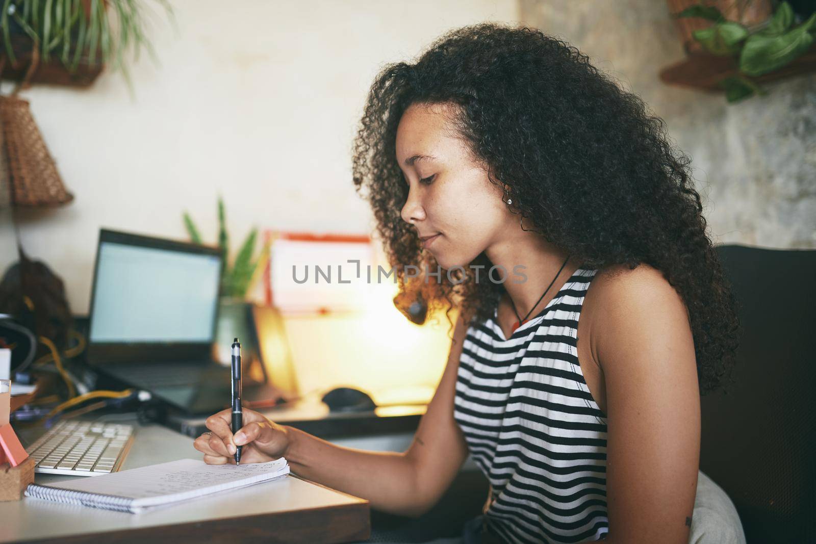 Shot of an attractive young african woman sitting alone and making a note in her home office - Stock photo