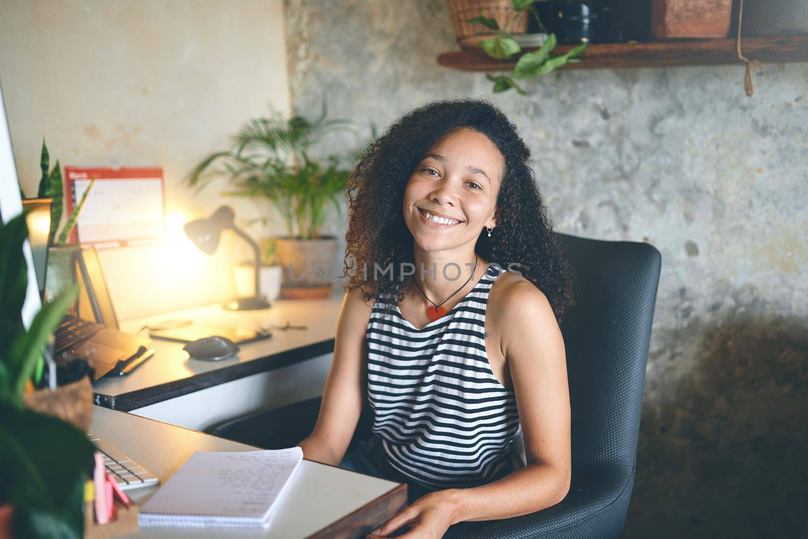 Shot of an attractive young woman sitting at her desk smiling at the camera - Stock Photo