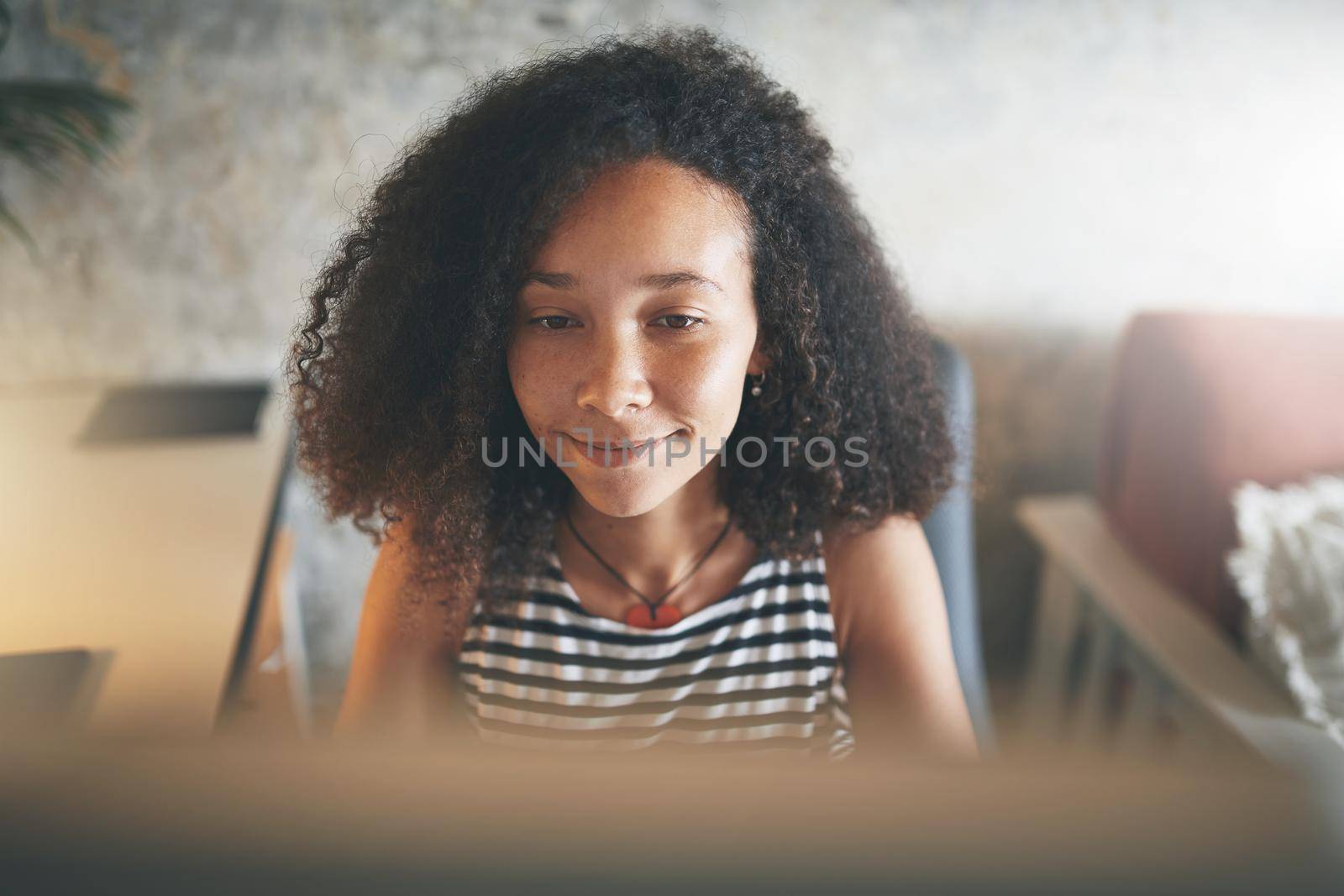 Shot of an attractive young african woman sitting alone and using her computer to work from home stock photo