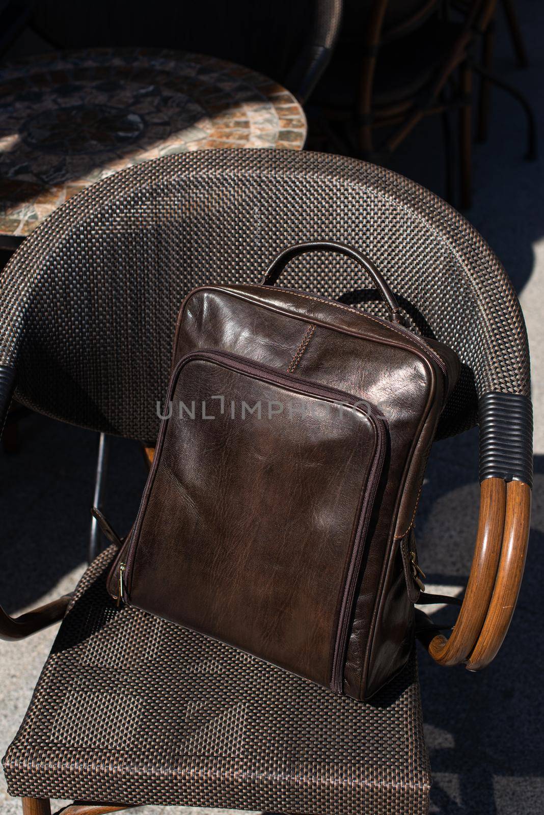 Brown leather backpack on the stylish chair. Outdoor photo