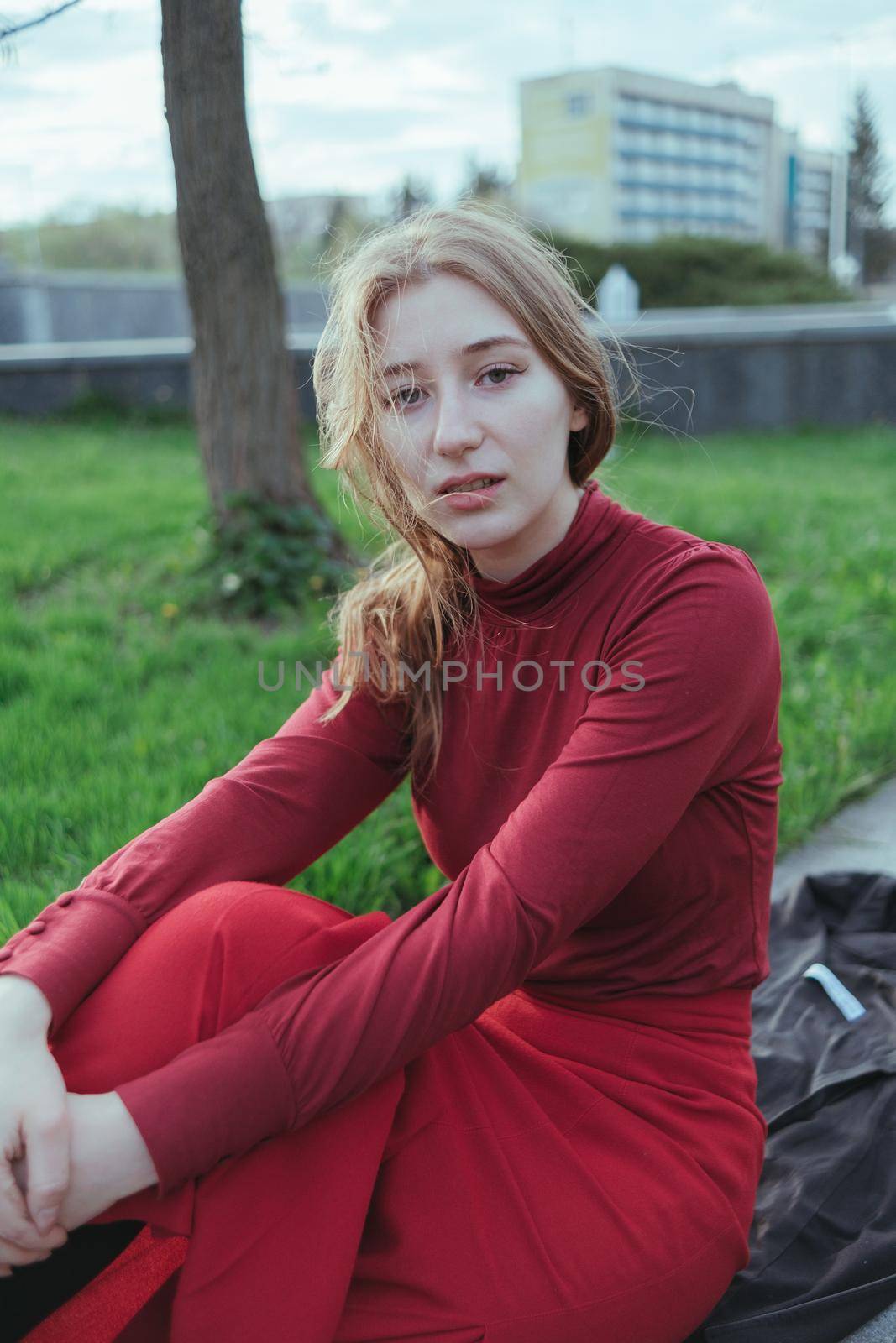 a blonde girl in red sits in the city, her hair is developed by the wind by Symonenko