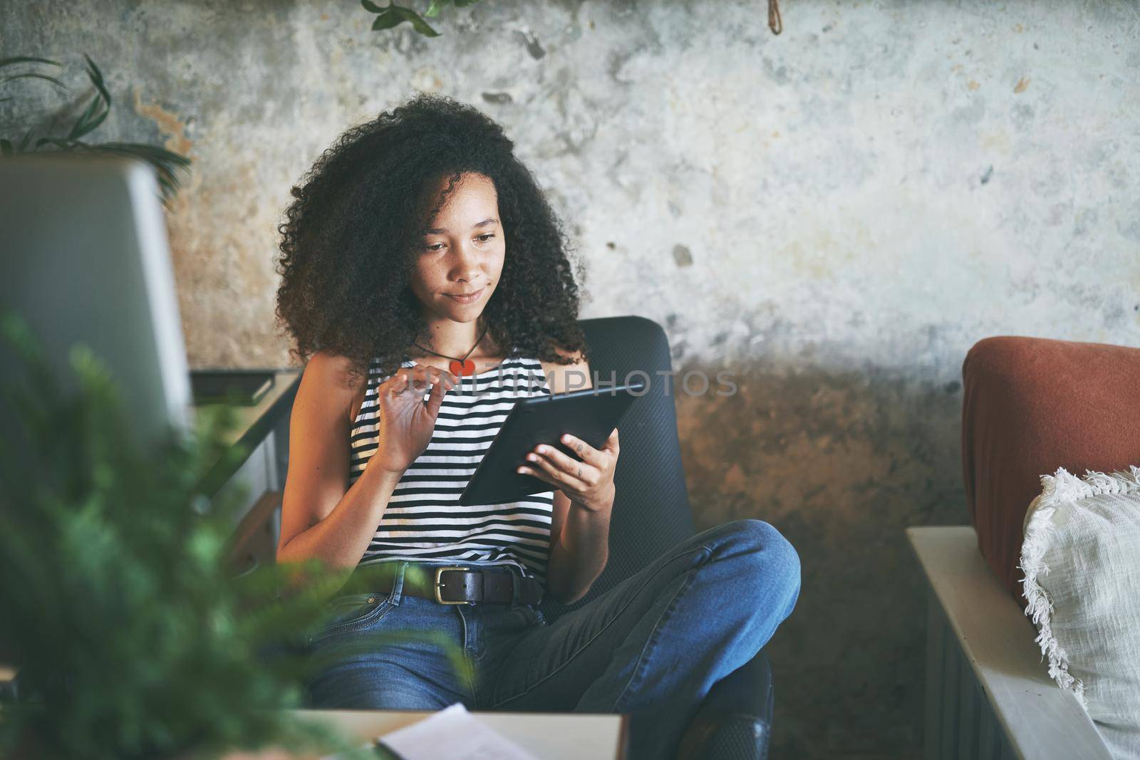 Shot of an attractive young african woman sitting alone and using her tablet while working from home stock photo