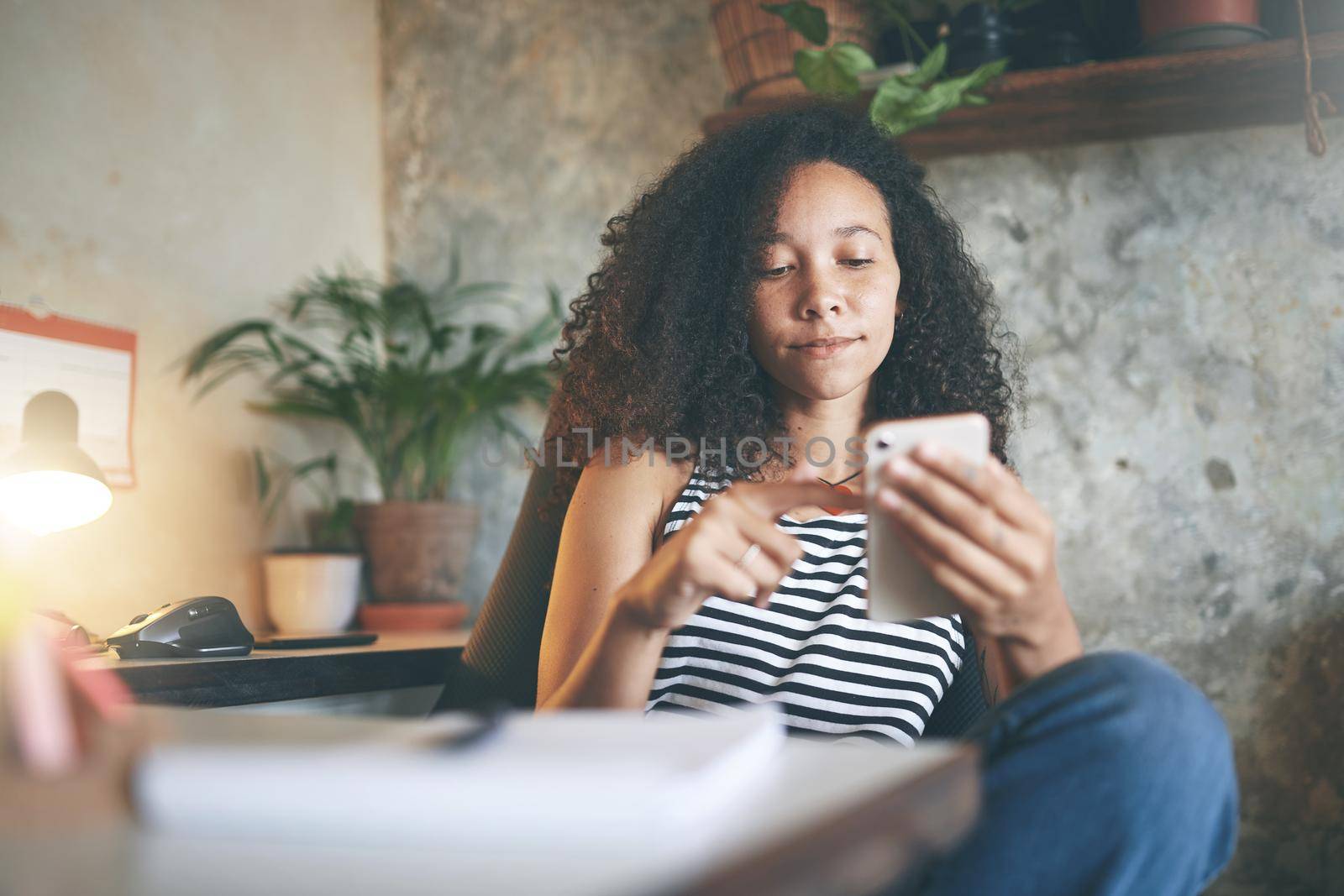 Shot of an attractive young african woman sitting alone and using her cellphone while working from home stock photo