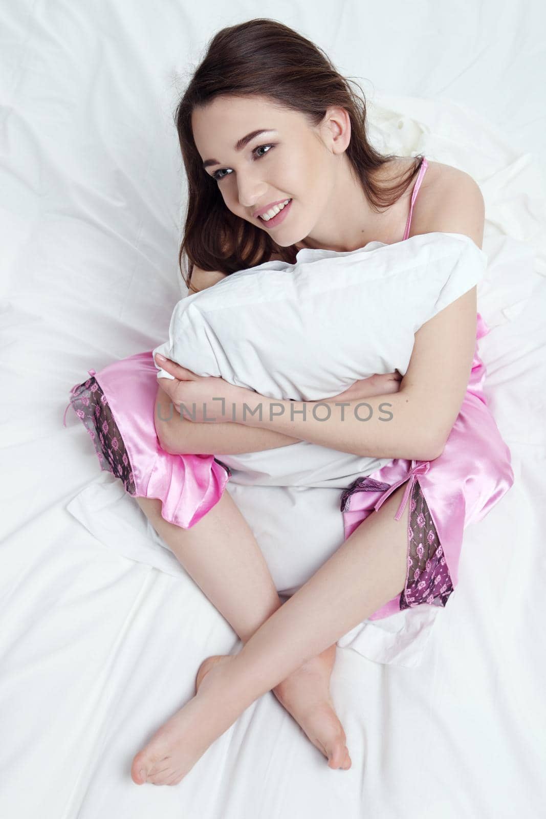 Beautiful young woman with attractive smile sitting embracing pillow