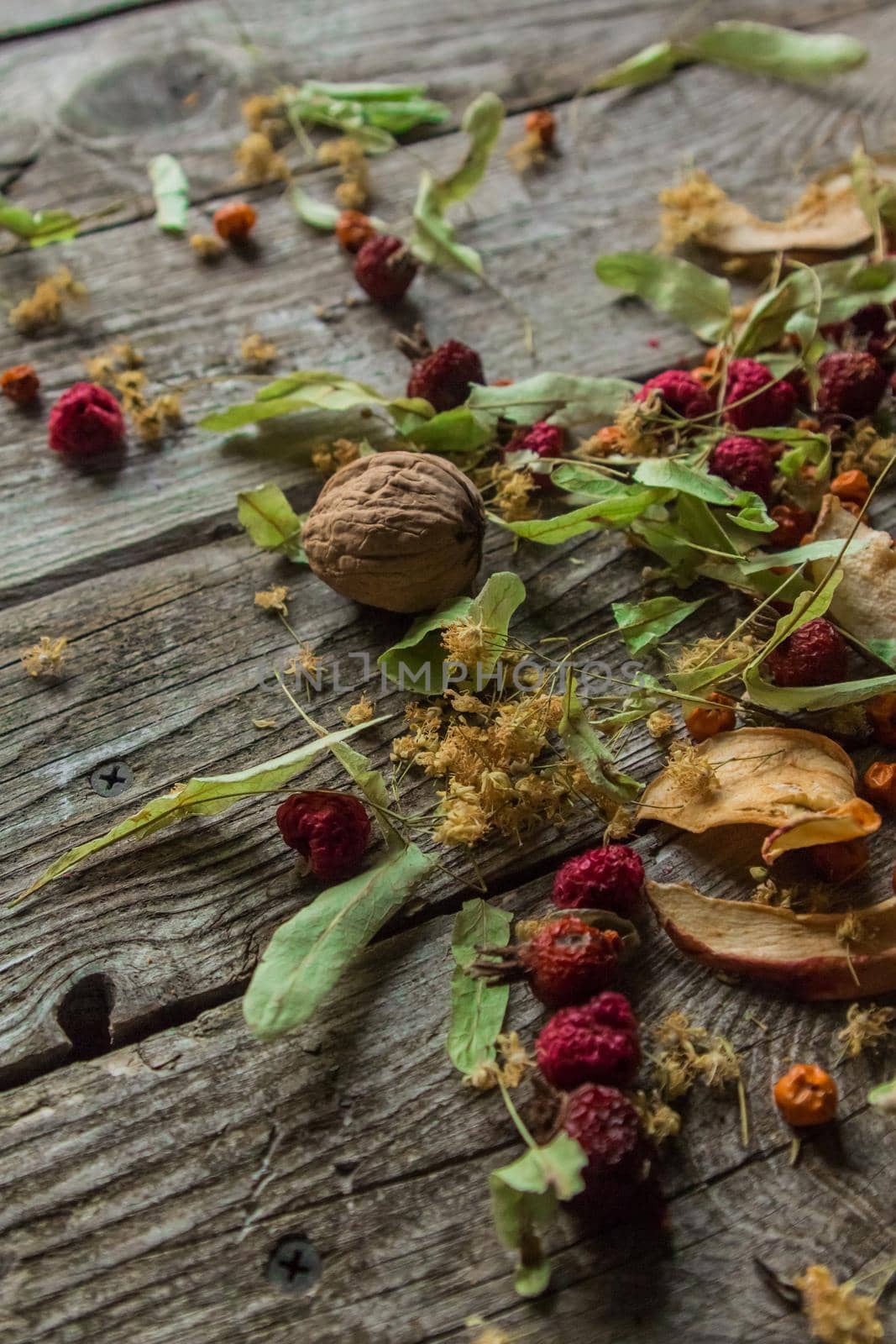 Dried delicious delicacies. Dry pieces of linden, rose hips, pears, raspberries, apples and walnuts snack on a wooden background by AYDO8