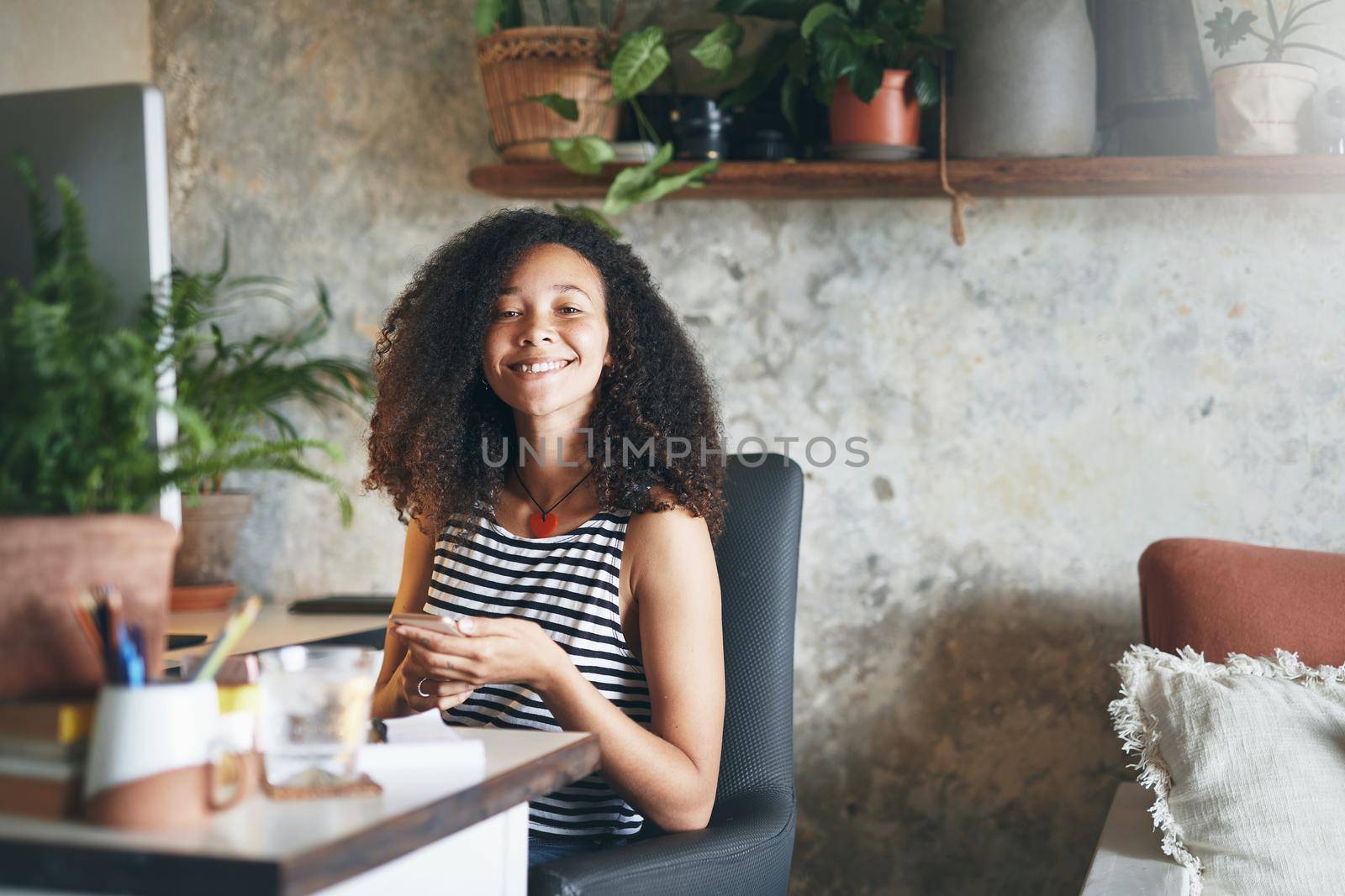 Shot of an attractive young african woman sitting alone and using her smartphone to work from home stock photo
