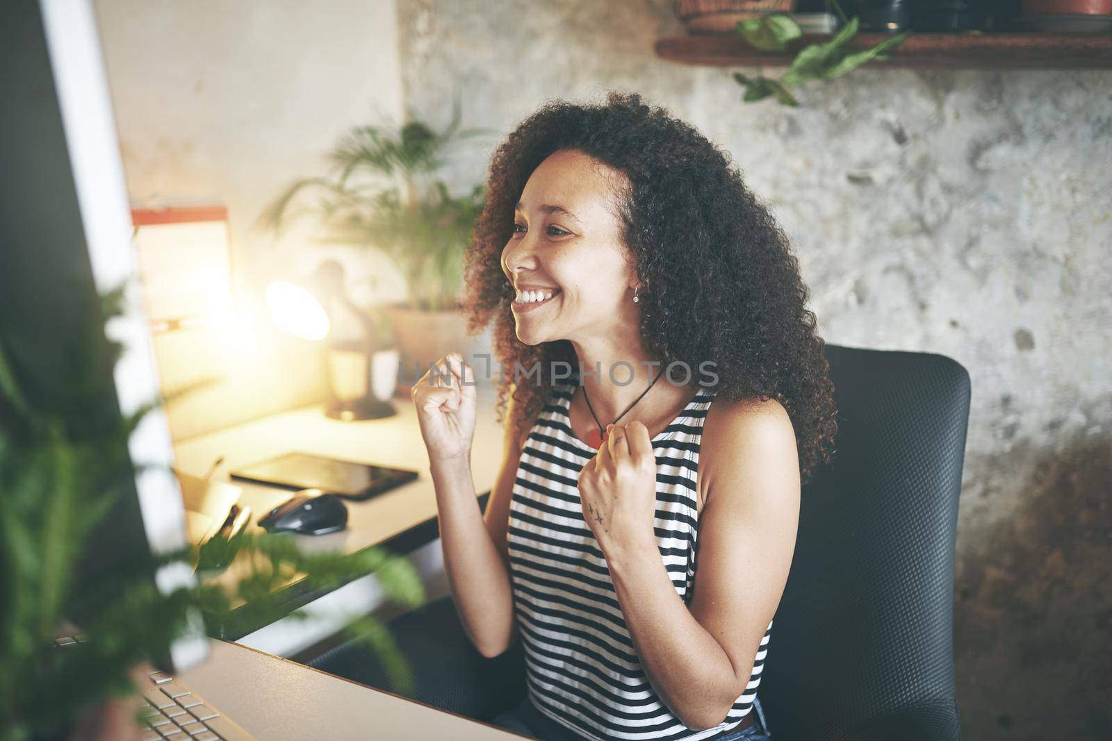 Shot of an attractive young african woman sitting alone and celebrating a success while using her computer to work from home stock photo