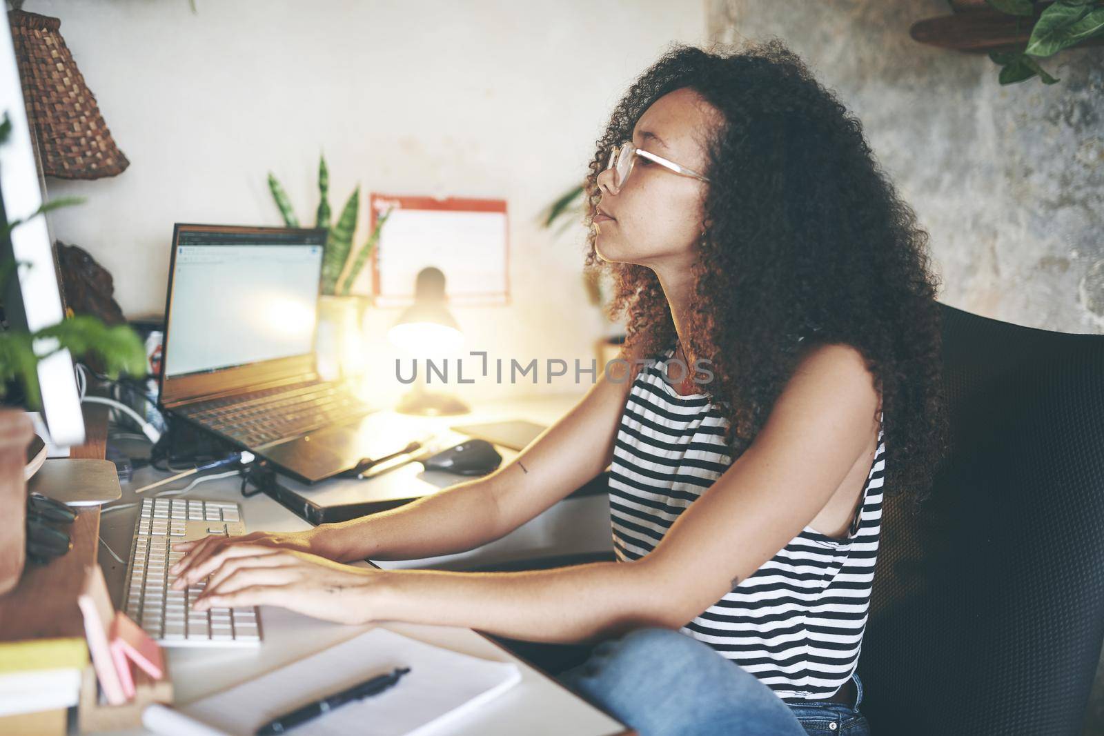 Shot of an attractive young african woman sitting alone and using her desktop pc while working from home stock photo