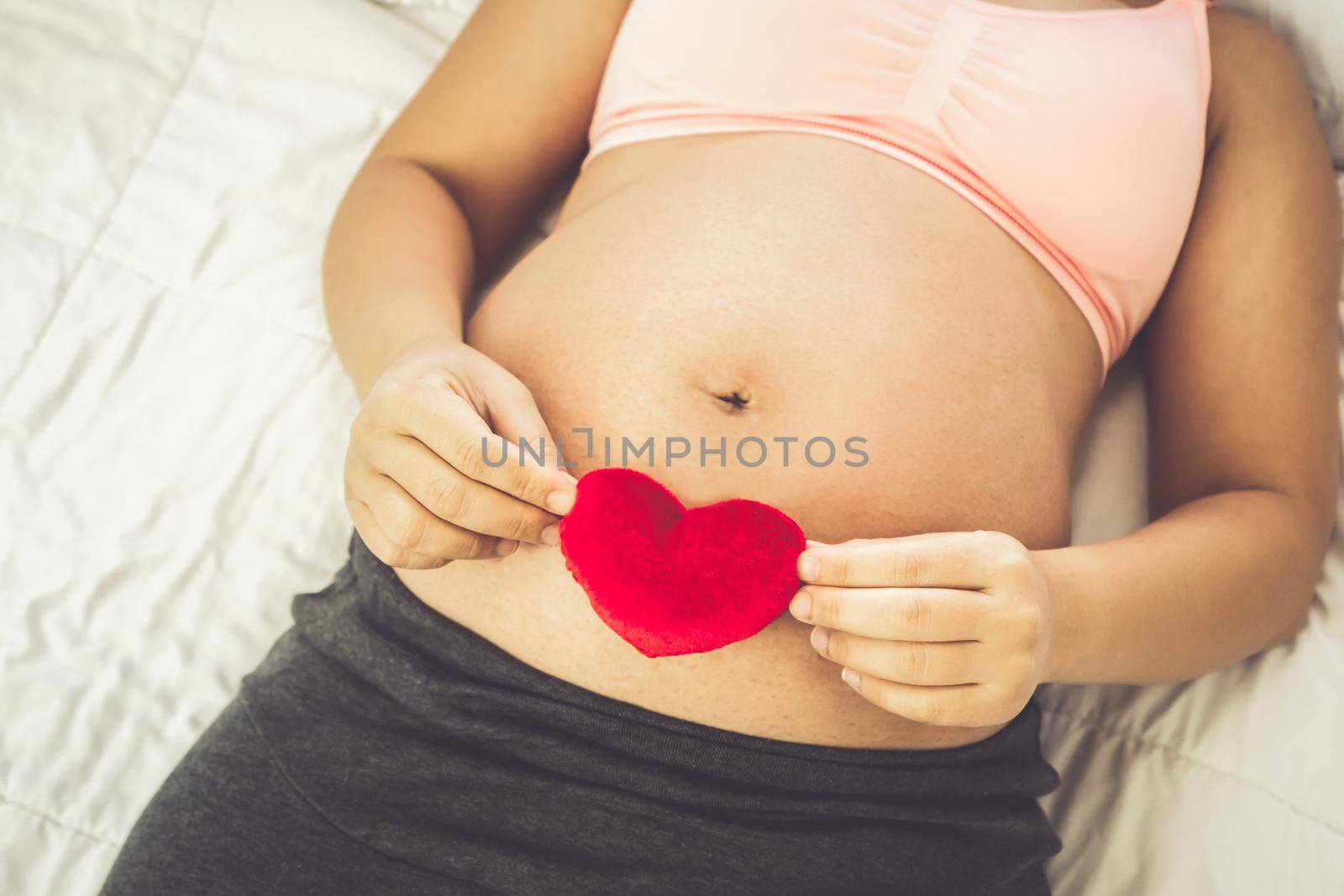 Pregnant woman feeling happy at home while taking care of her child. The young expecting mother holding baby in pregnant belly. Maternity prenatal care and woman pregnancy concept.