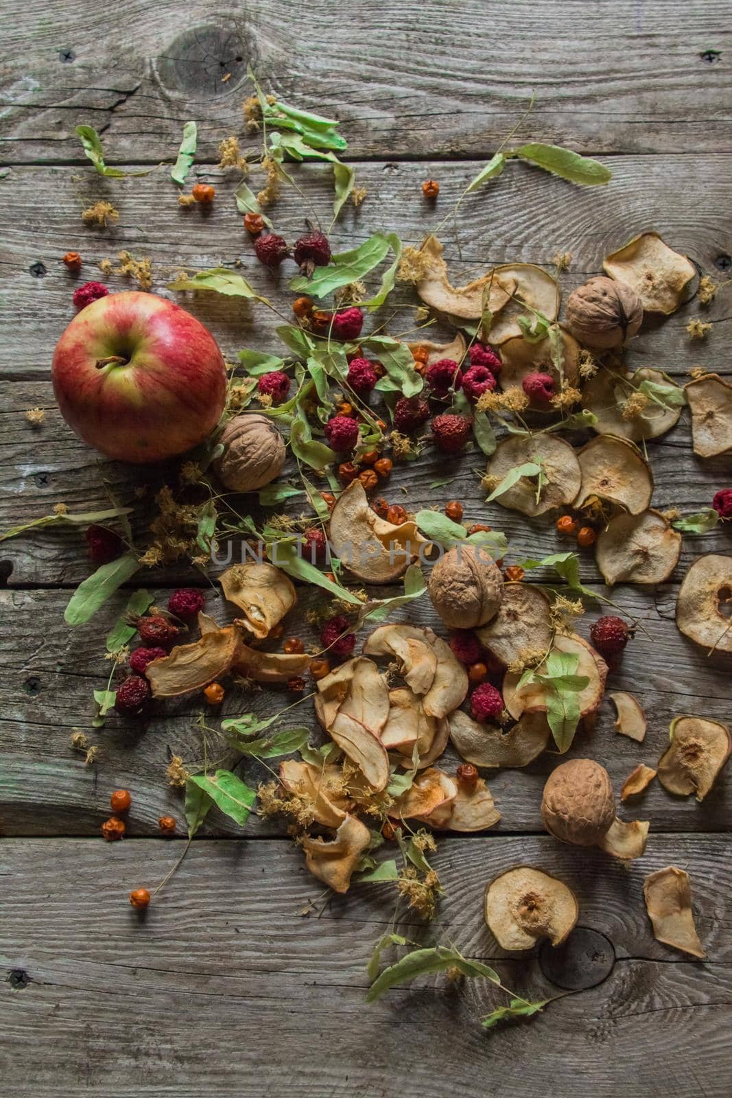 Dried delicious delicacies. Dry pieces of linden, rose hips, pears, raspberries, apples and walnuts snack on a wooden background by AYDO8