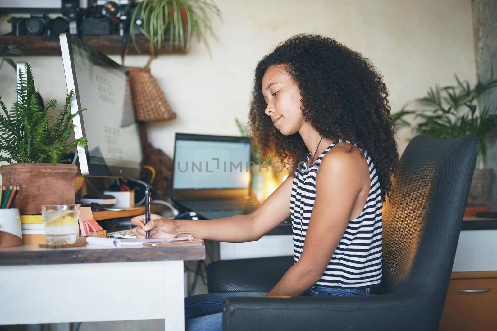 Shot of an attractive young african woman sitting alone and making notes in her home office - stock photo