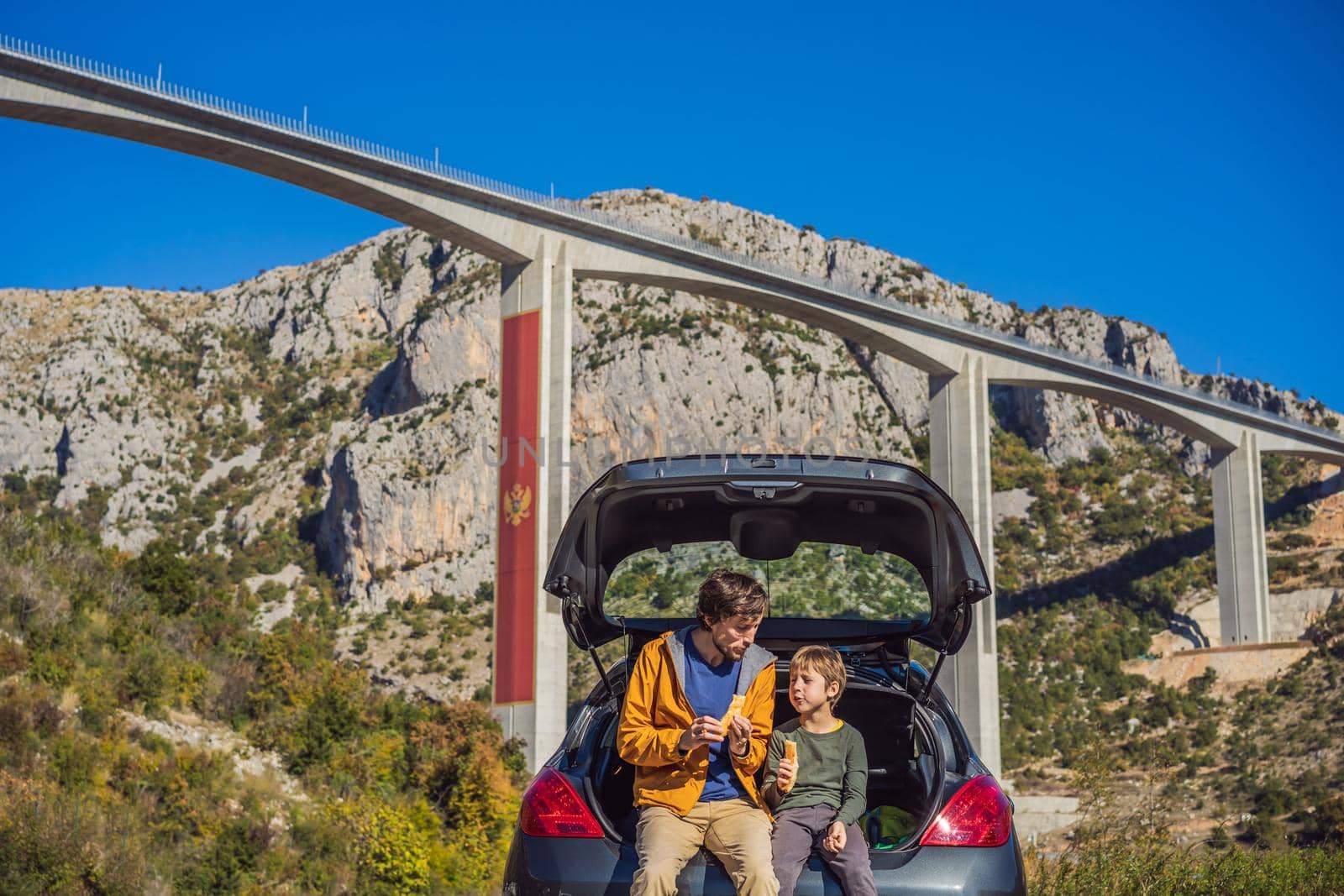 Montenegro. Dad and son tourists are sitting on the trunk of a car. Road trip around Montenegro. Bridge Moracica. Reinforced concrete bridge across the Moraci gorge. The motorway Bar - Bolyare. The bridge is on the Smokovac - Uvach - Mateshevo section. The Moracica Bridge was built by the China Road and Bridge Corporation by galitskaya