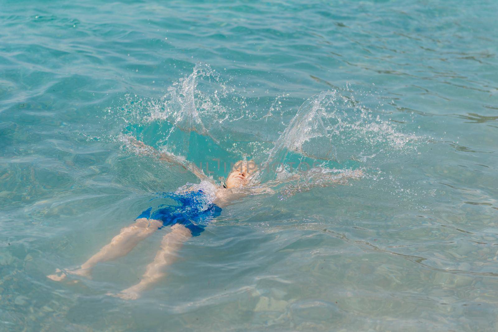 Child learning to swim in the open sea of tropical resort. Kids learn swimming. Exercise and training for young children. Little boy with colorful float board in sport club. Swimming baby or toddler. Happy child boy swims in sea in swimming circle with splash. Blue sky and water. Swimming training. Fun joy activities on vacation in the beach. Childhood moments lifestyle. Freedom careless. boy swim in the sea by Andrii_Ko