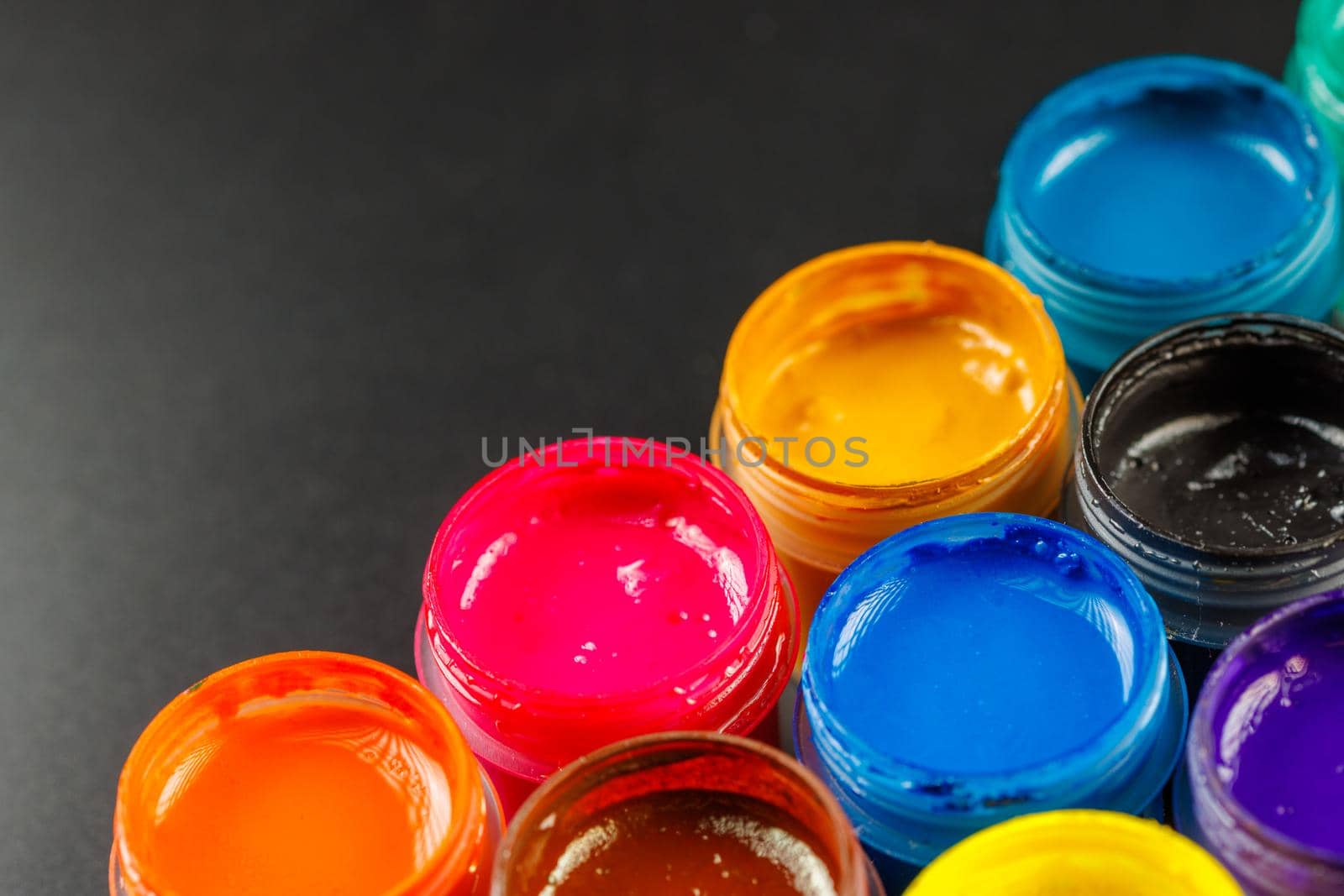 close-up background of opened small gouache paint jars on black surface by z1b