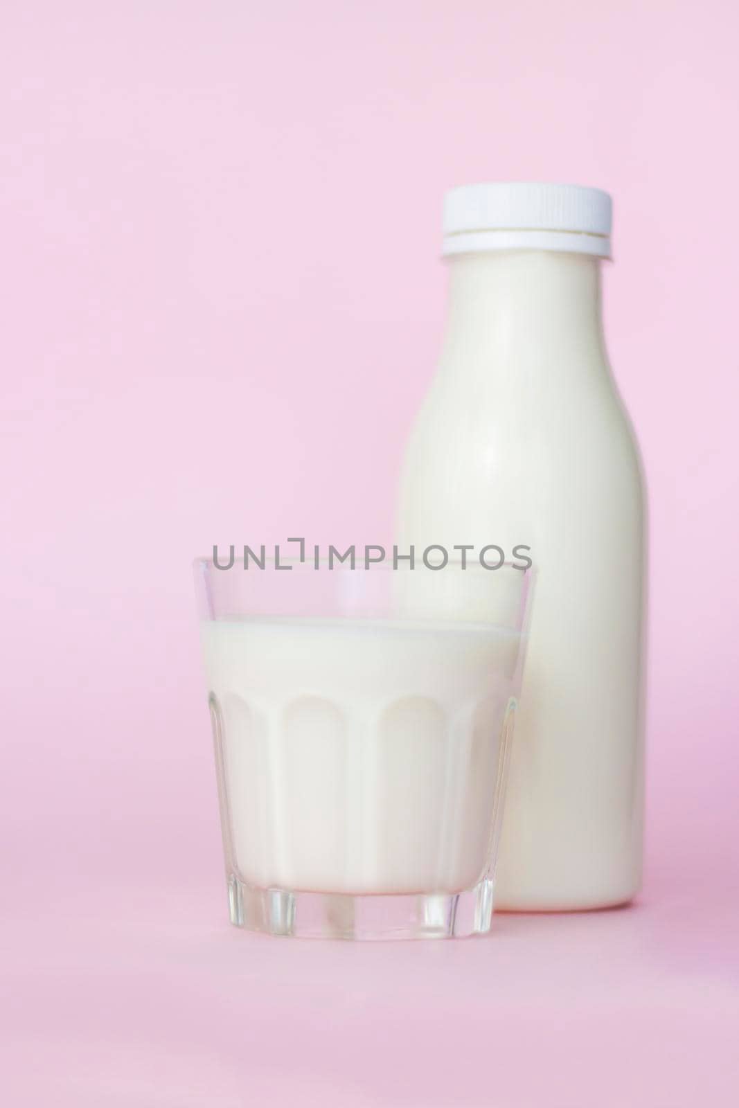 A bottle and a glass of white milk, highlighted on a pink background, close-up. Dairy product concept, copy space