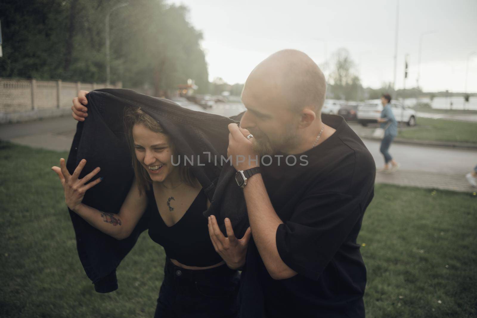 a couple in love is fleeing the rain. the guy covers the girl with his jacket by Symonenko