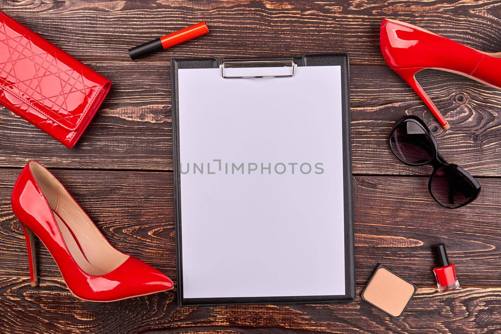 Clipboard with blank paper and red accessories. Brown wooden desk background.