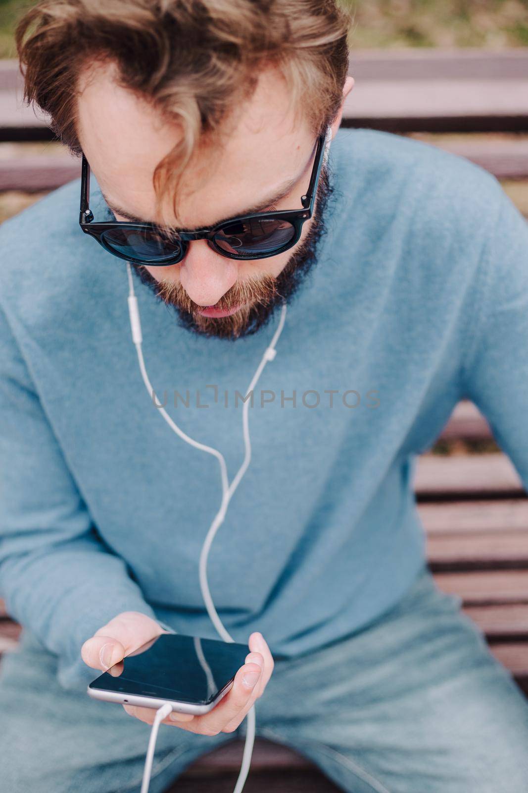 young hipster gay man listening music with headphones siting in a park
