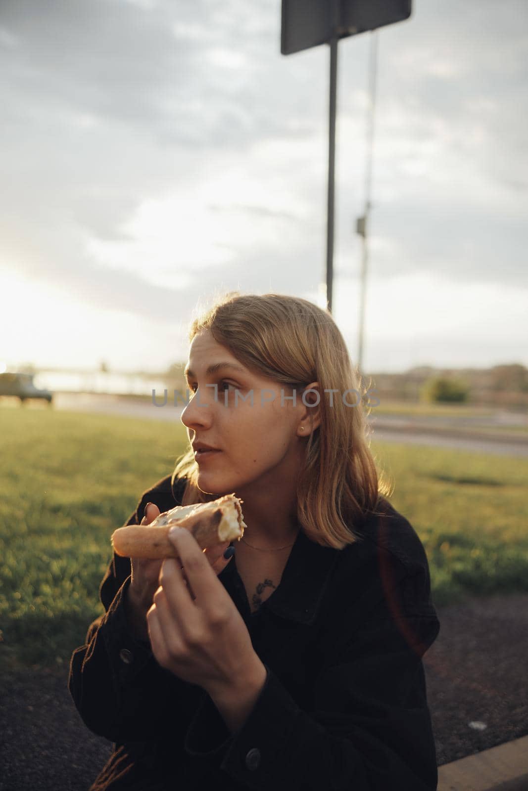 blonde girl eating pizza sitting outside at sunset